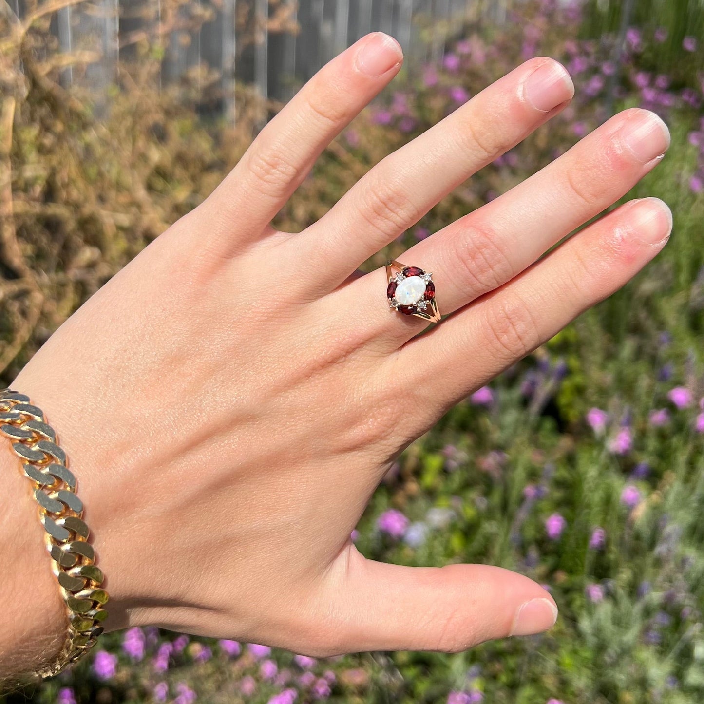 A ladies natural opal ring in yellow gold. The opal is surrounded by red marquise cut garnets and diamonds.