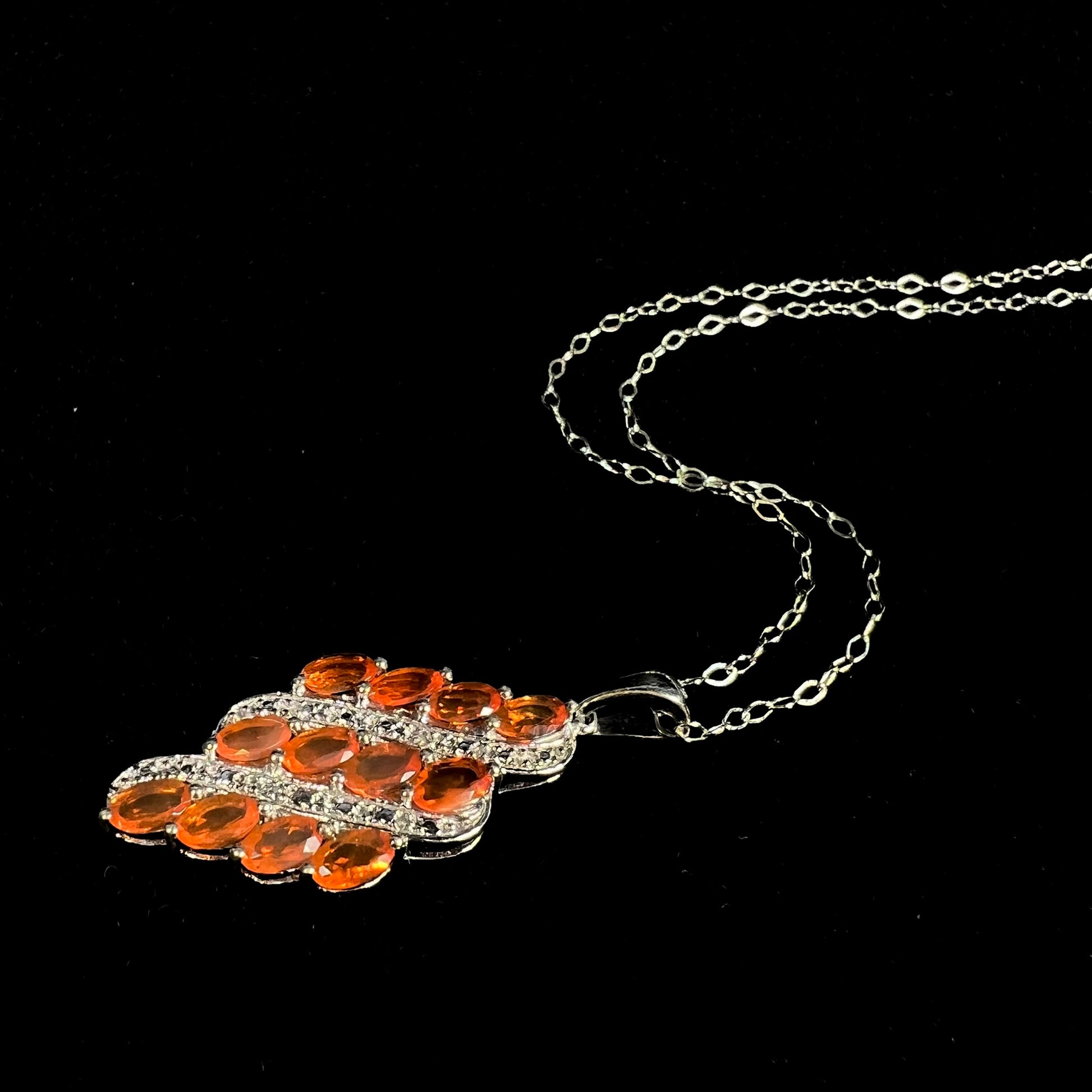 An orange fire opal necklace set with a cluster of Mexican fire opals, laying against a black background.
