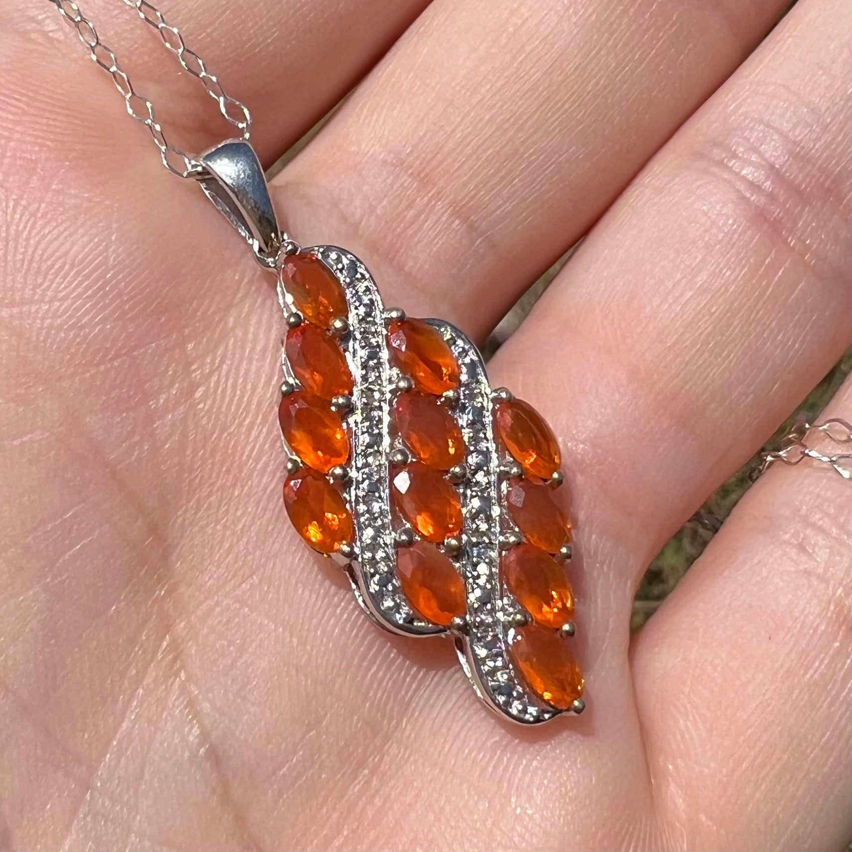 A sterling silver Mexican fire opal necklace featuring a cluster of faceted orange fire opals, shown in sunlight.