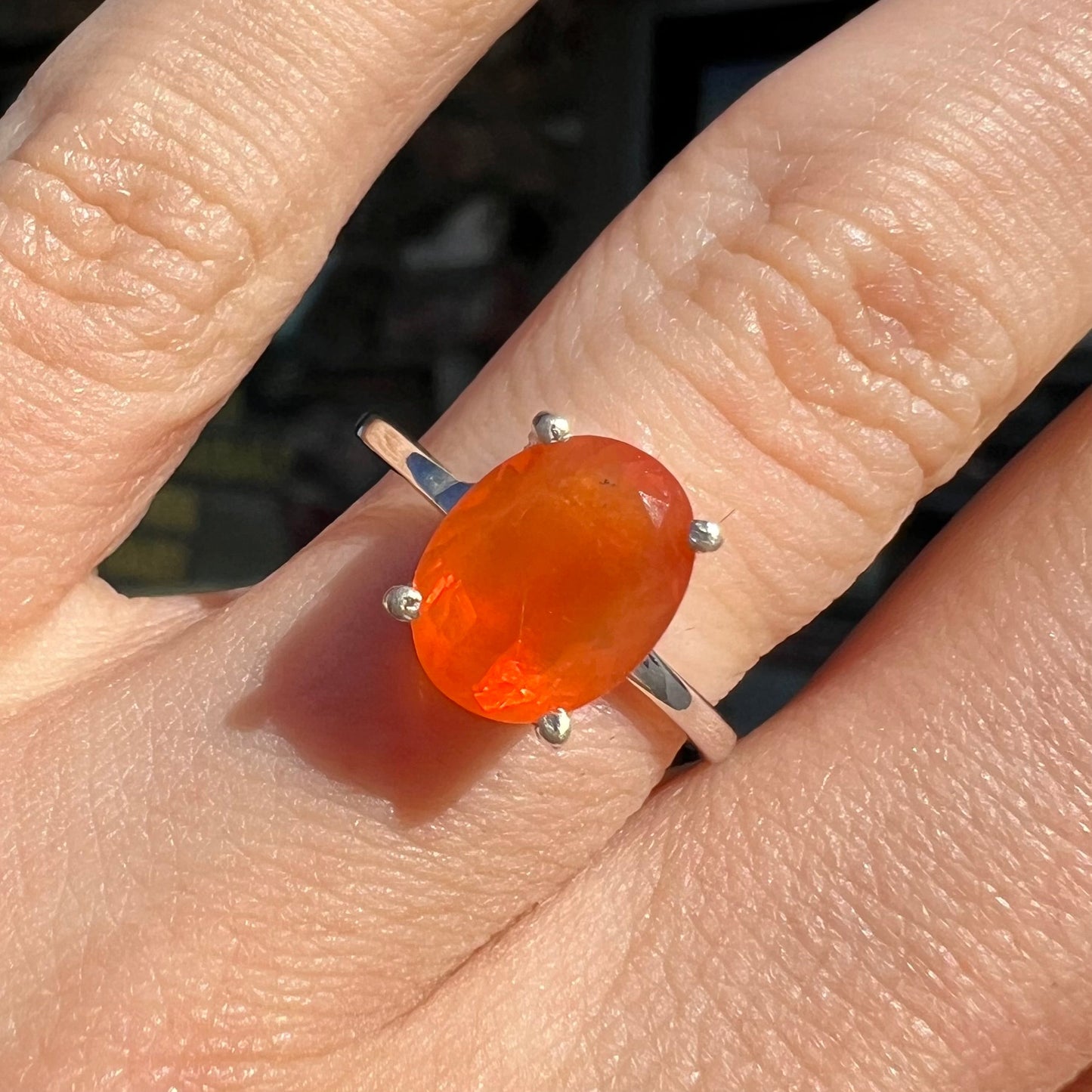 A silver solitaire ring set with a natural, faceted oval cut Mexican fire opal. The stone is a bright orange color.