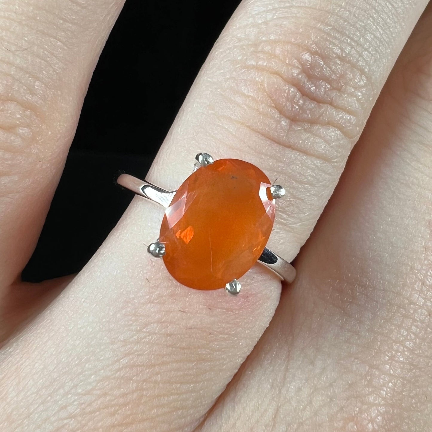 A silver solitaire ring set with a natural, faceted oval cut Mexican fire opal. The stone is a bright orange color.