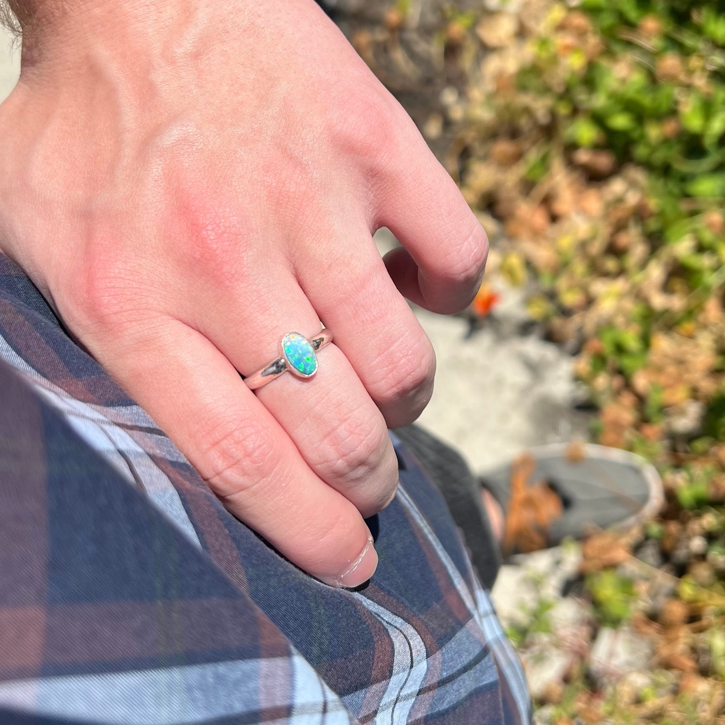 Close-up of hand resting on hip in sunlight while wearing a sterling silver women's ring set with a blue Australian opal.