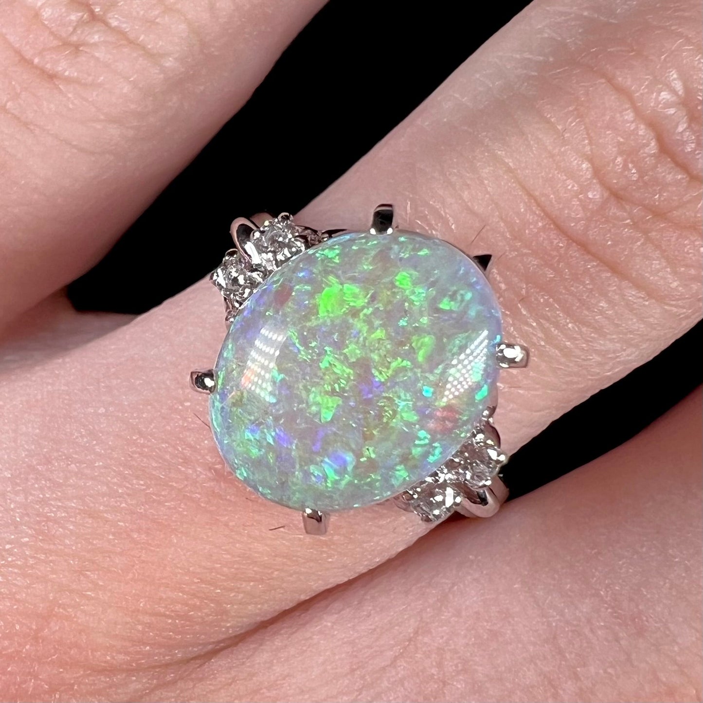 An Australian crystal opal and diamond engagement ring set in a platinum filigree mounting. The opal plays green/blue colors and has a crack.