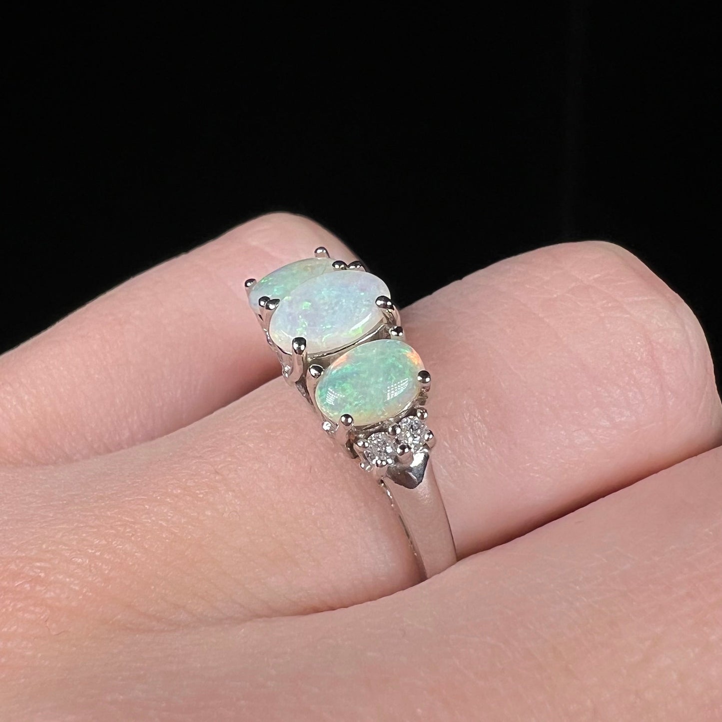 A ladies' white gold ring prong-set with three natural white opals and diamond accents. The opals play a green color.