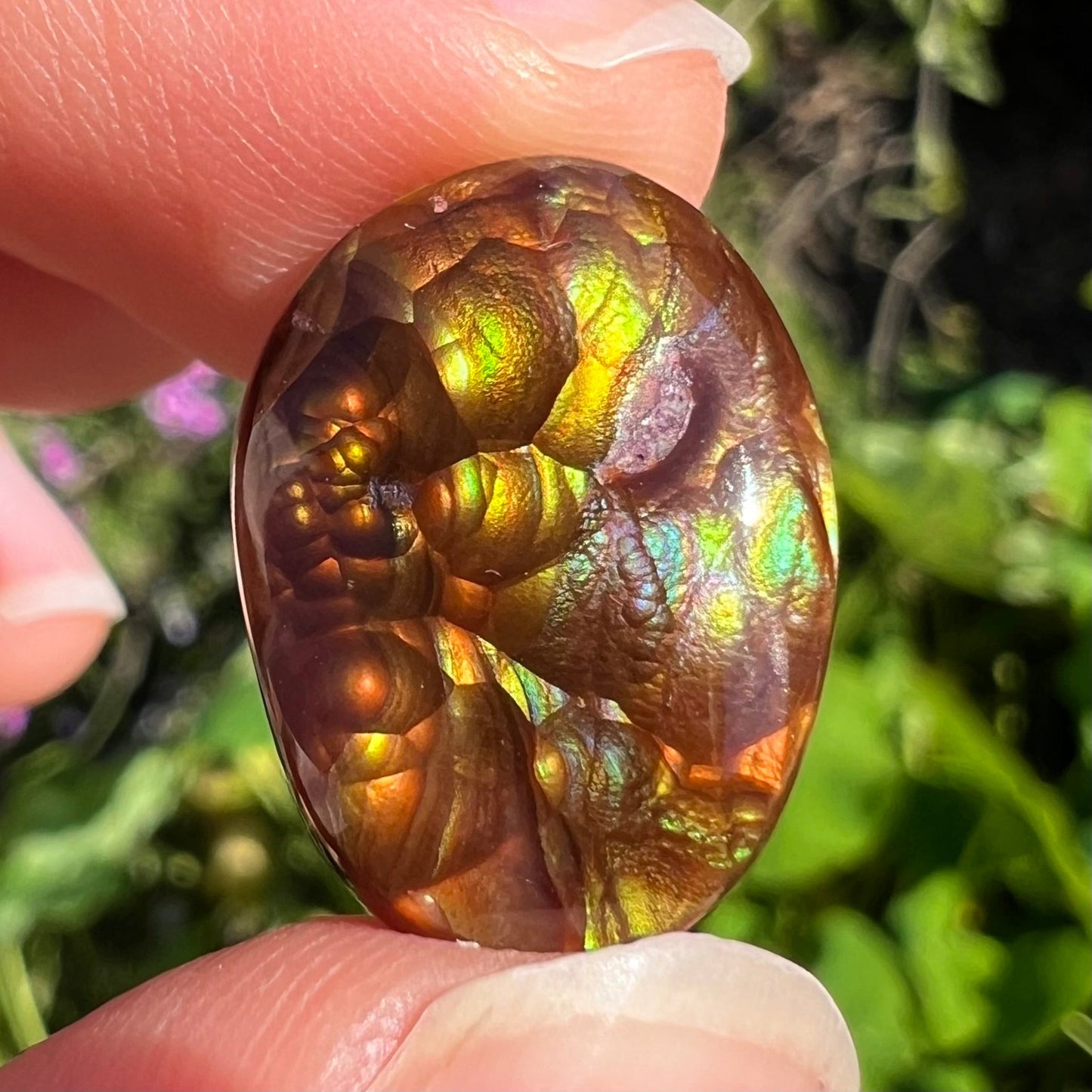 An oval cabochon cut Mexican fire agate stone. The stone's predominant colors are green, yellow, orange, and blue.