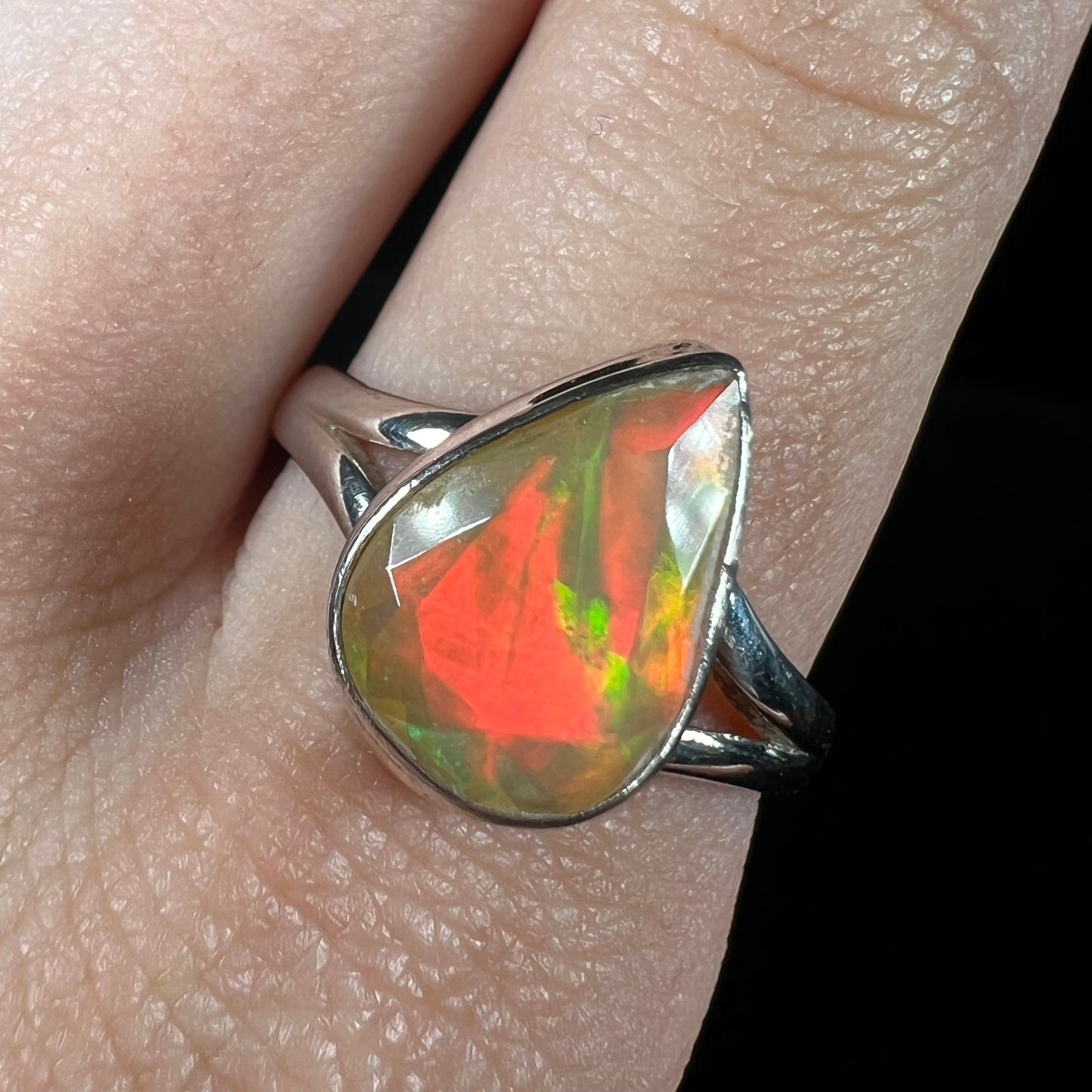 A unisex sterling silver ring set with a faceted pear shaped Ethiopian fire opal. The opal plays orange, red, and green colors.