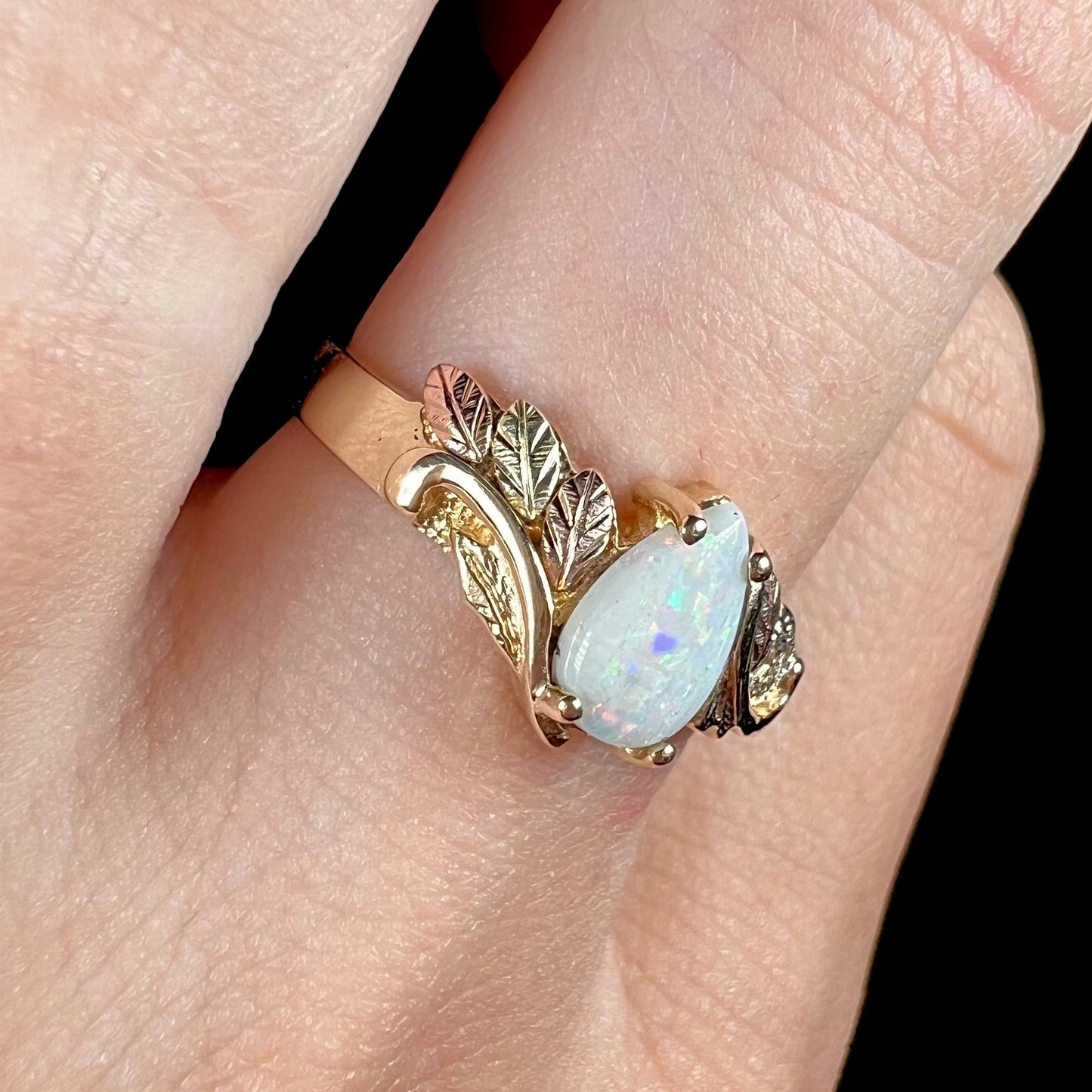 A ladies' two-tone yellow and rose Black Hills gold opal and diamond ring. The opal is a pear shaped cabochon.