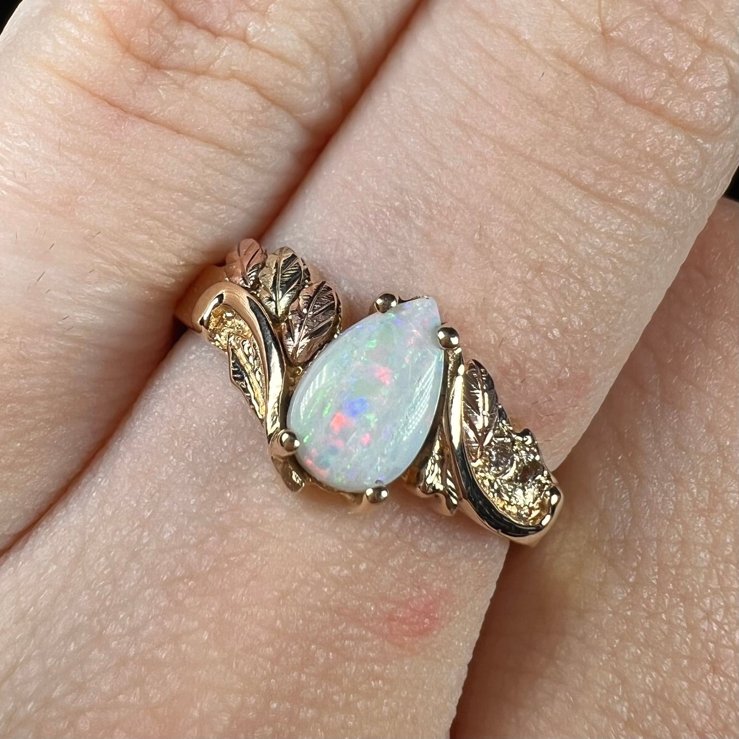 A ladies' two-tone yellow and rose Black Hills gold opal and diamond ring. The opal is a pear shaped cabochon.
