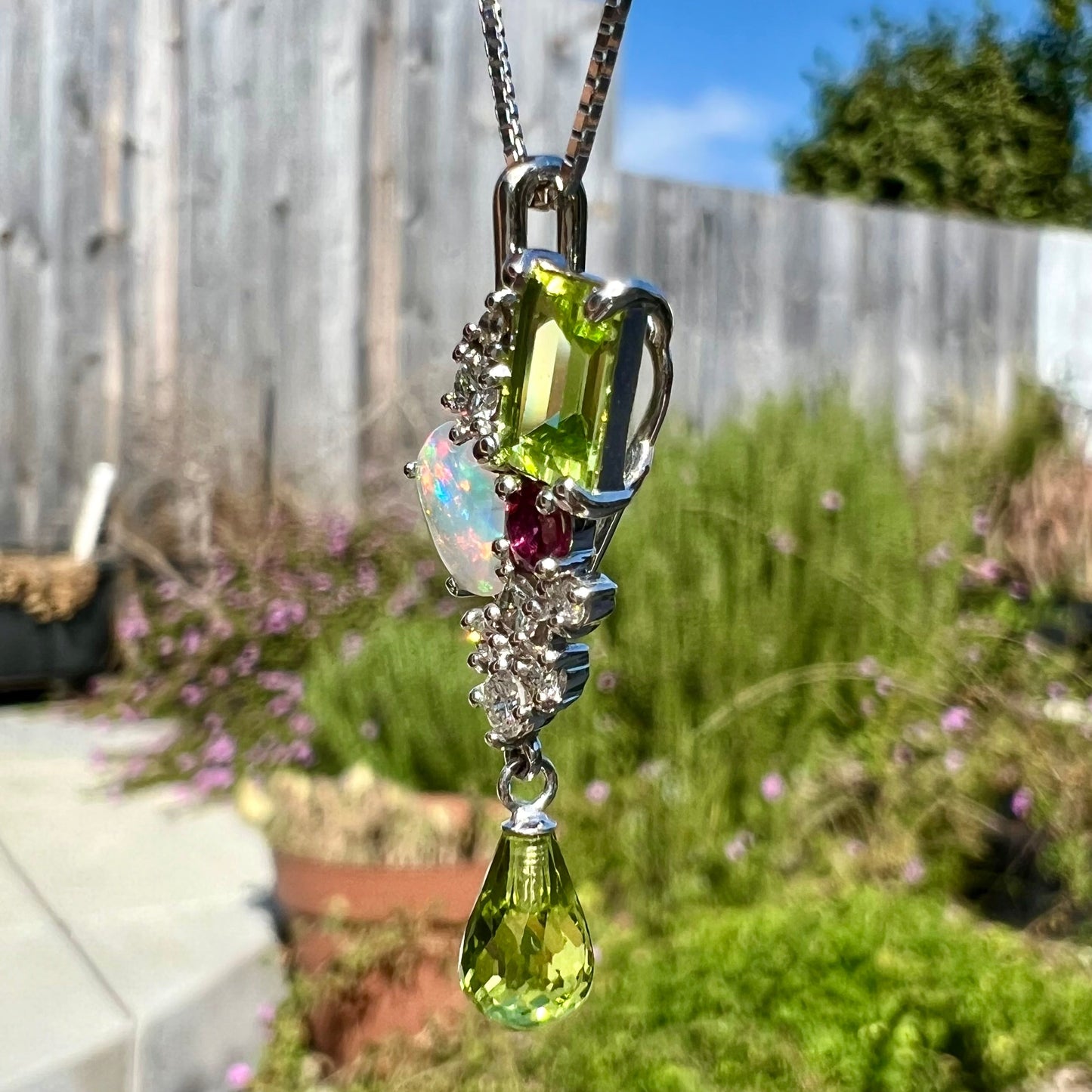 A ladies' white gold cluster gemstone necklace mounted with peridot, diamonds, purple sapphire, and an opal.