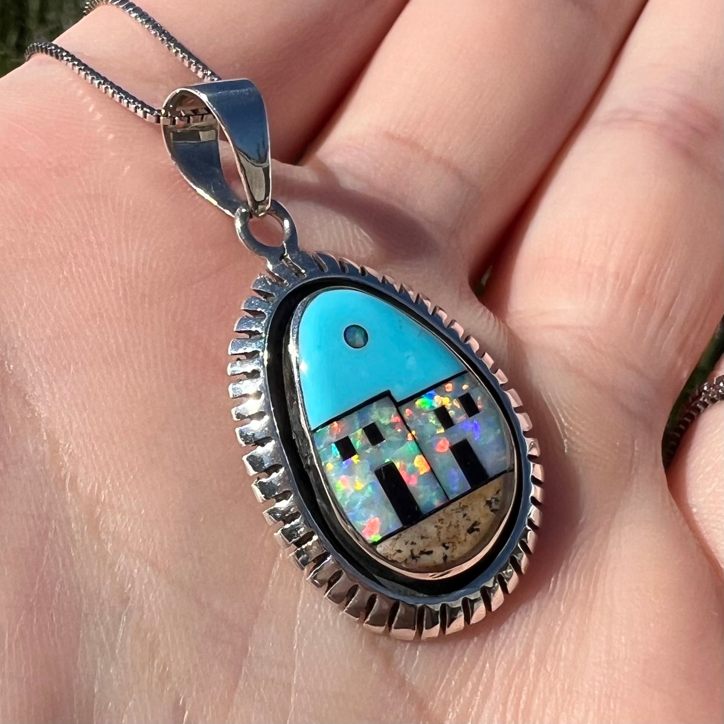 A Philippines-made Southwest-style silver opal and turquoise inlay necklace, held at an angle in a hand in sunlight.