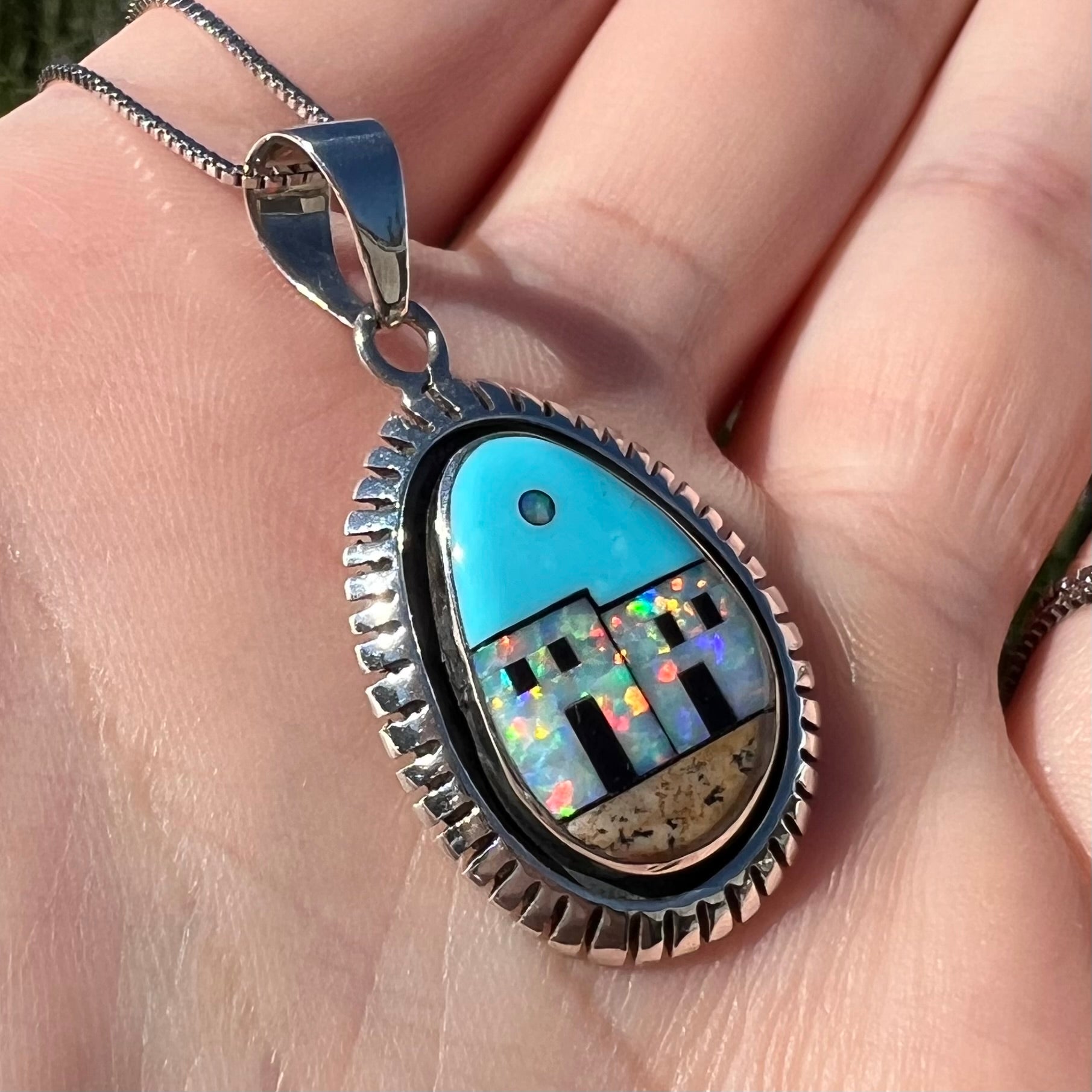 A Philippines-made Southwest-style silver opal and turquoise inlay necklace, held at an angle in a hand in sunlight.