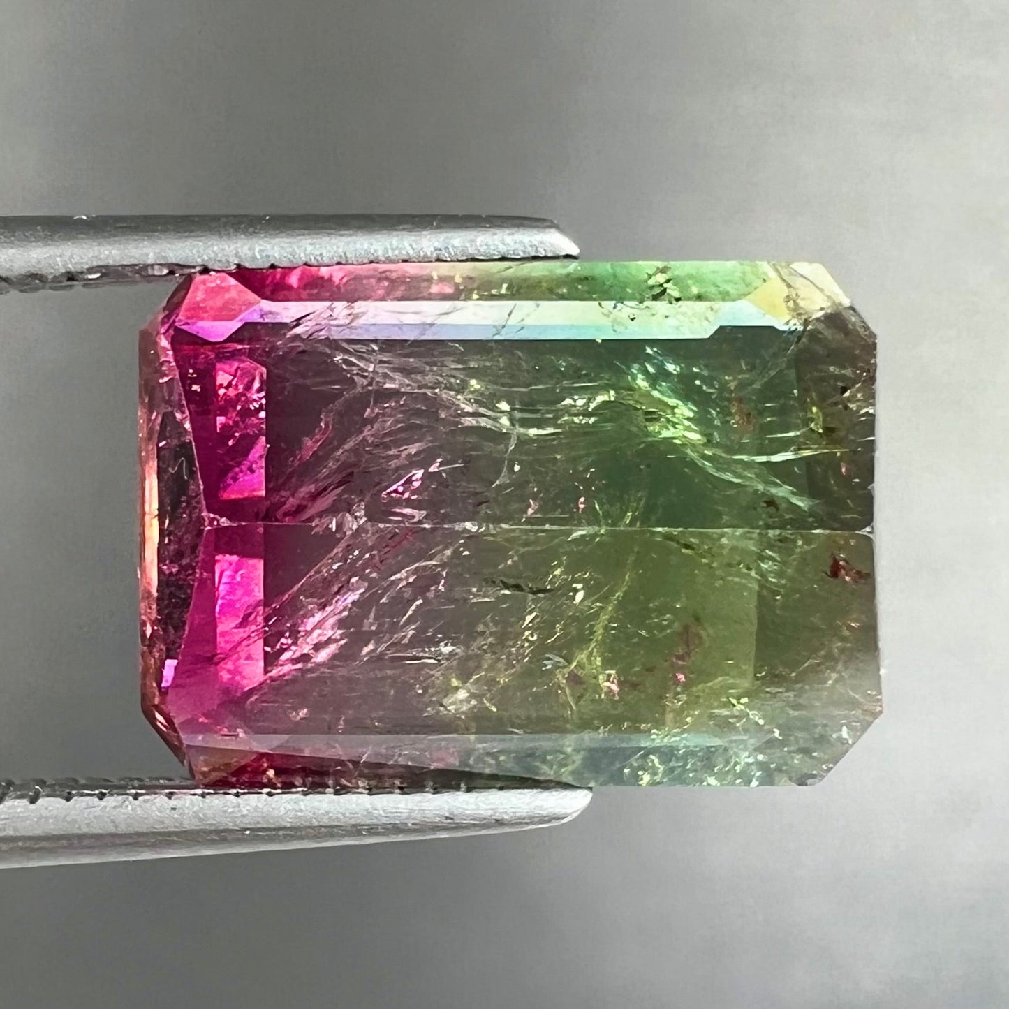 A loose watermelon tourmaline gemstone. The stone is emerald cut and fades from hot pink to green.