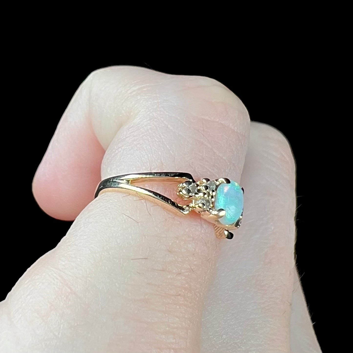 A ladies' yellow gold opal and diamond pinkie ring. The ring is a small size, and the opal shines green and blue colors.