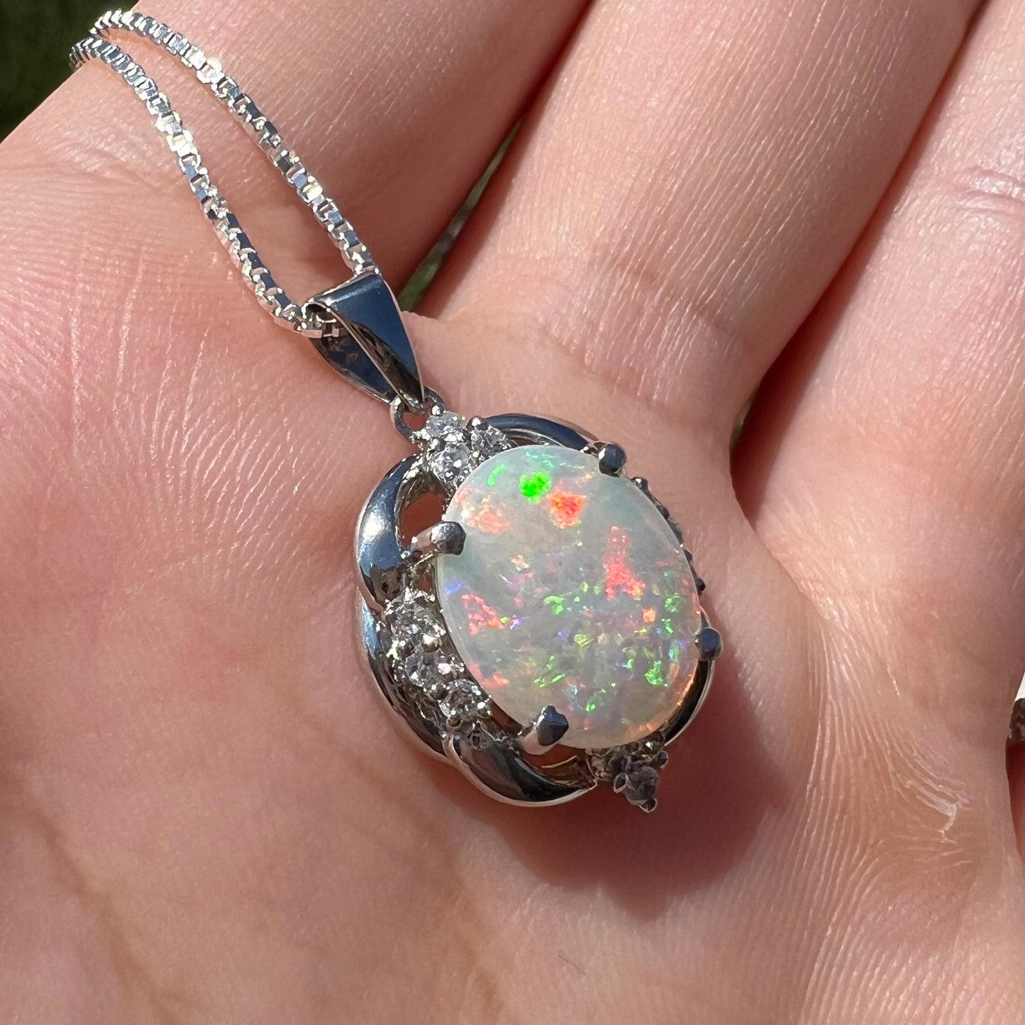 Angled view of a platinum Australian opal and diamond necklace held by a hand in the sunlight.