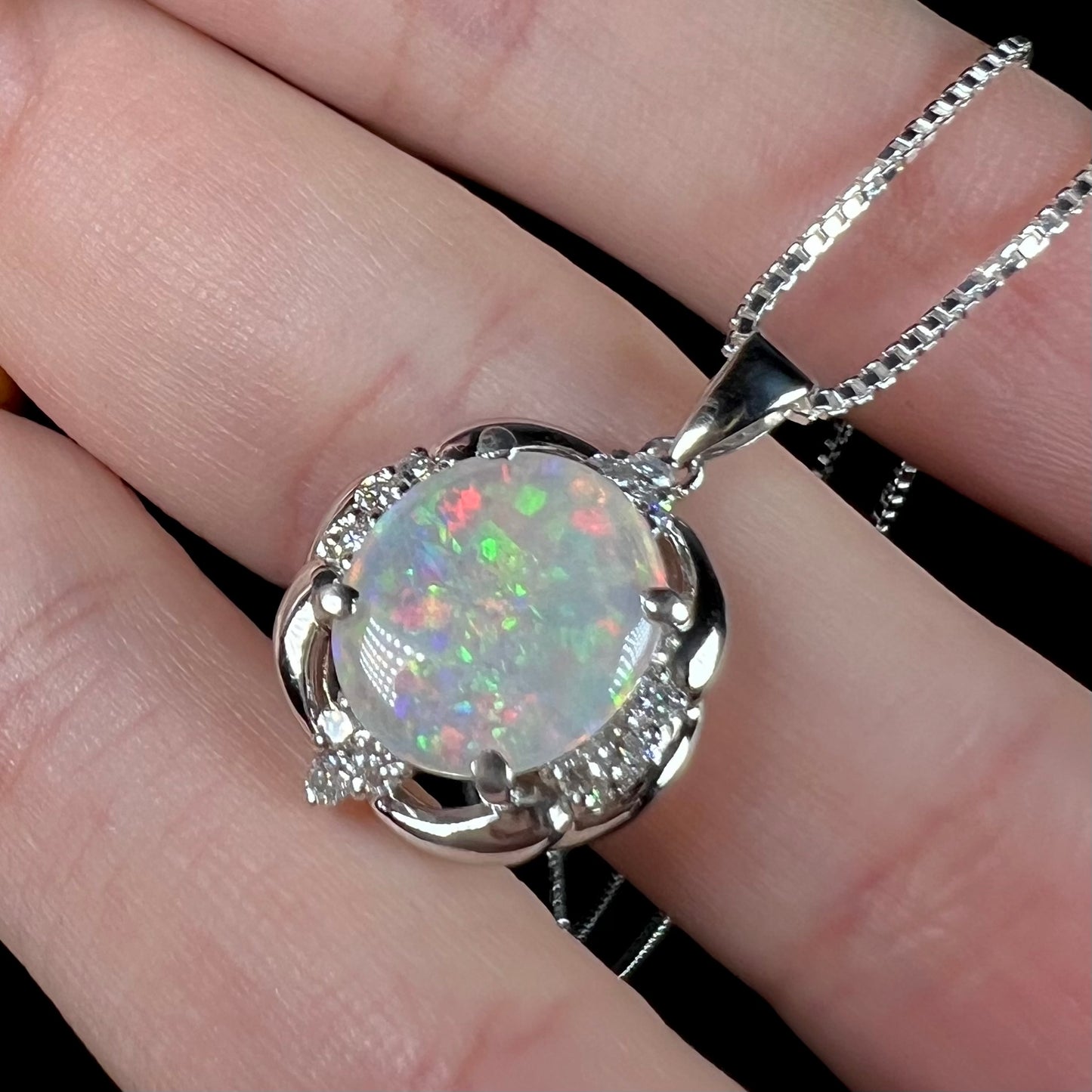 Macro shot of a platinum Australian opal necklace, held in a hand at an angle.
