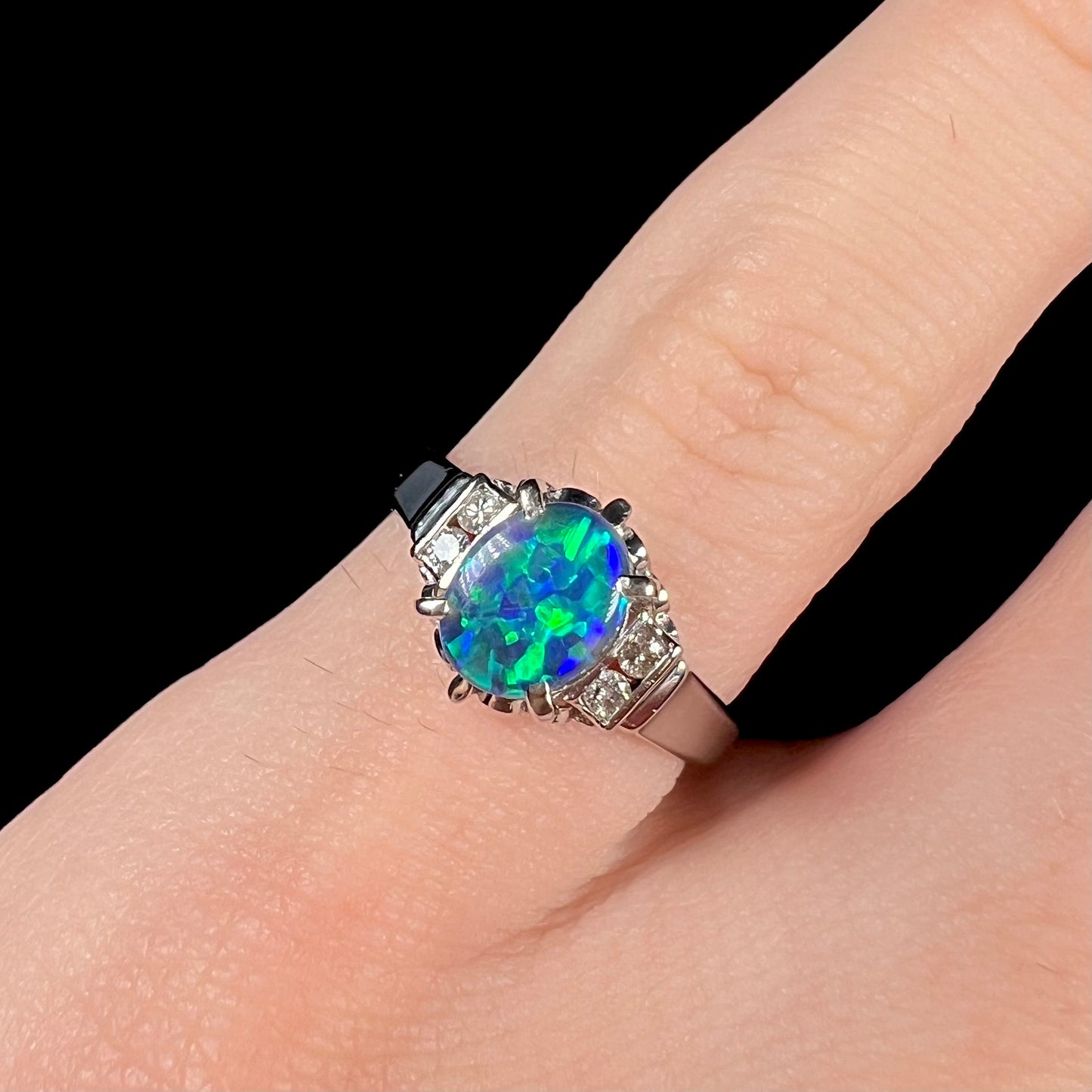 Vibrant green fire plays on a Lightning Ridge black opal, mounted on a platinum engagement ring with diamond accents.
