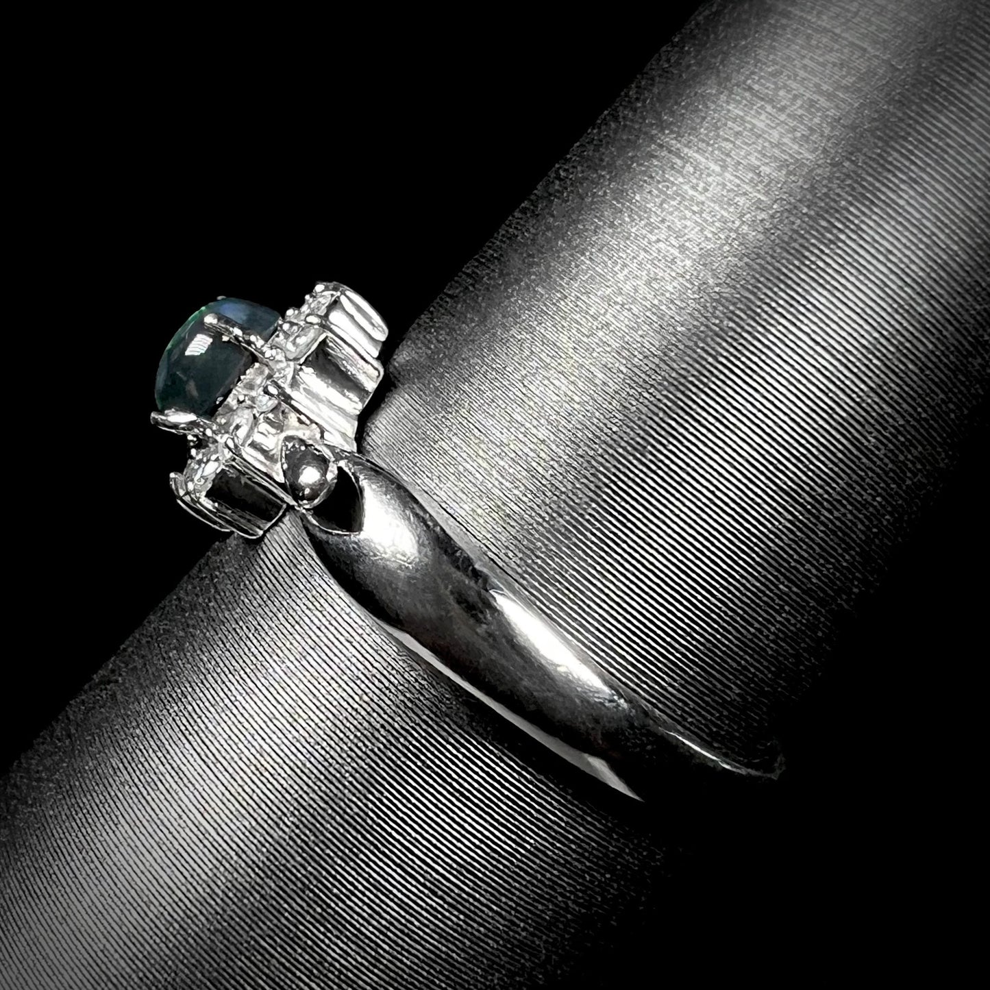 Side profile of black opal engagement ring with diamond halo and platinum band.