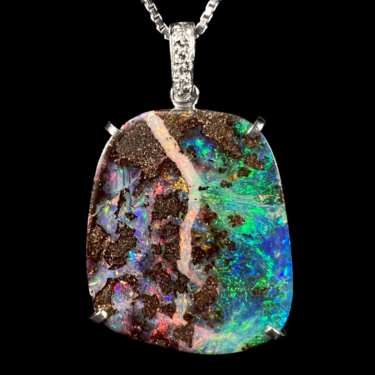 A platinum boulder opal and diamond pendant with highly saturated green, blue, and red fire, displayed against a black background.