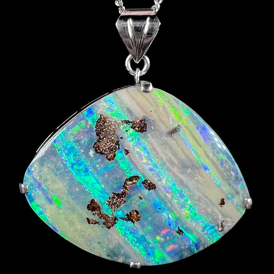Macro view of a platinum boulder opal necklace showing bright bands of green and blue fire against a black background.