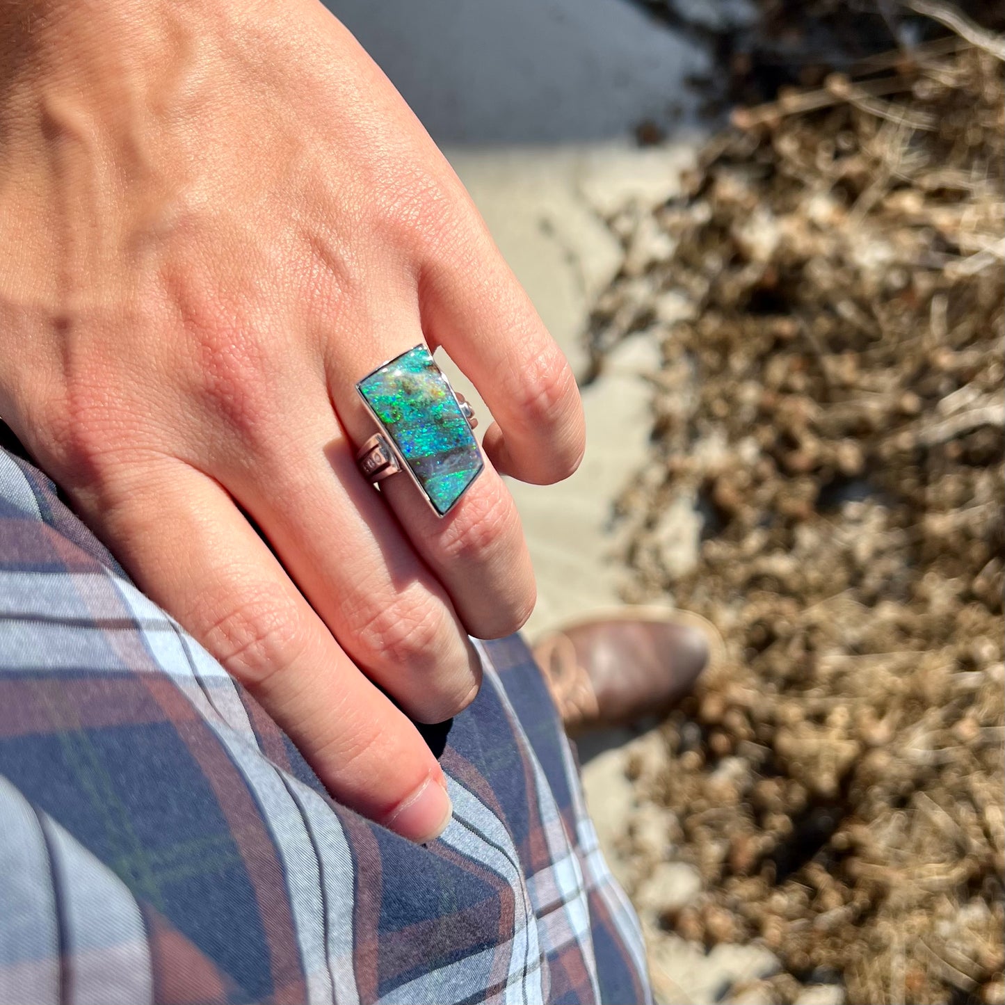 A platinum boulder opal and diamond ring with blue color play worn on a hand  as the hand rests on the model's hip.