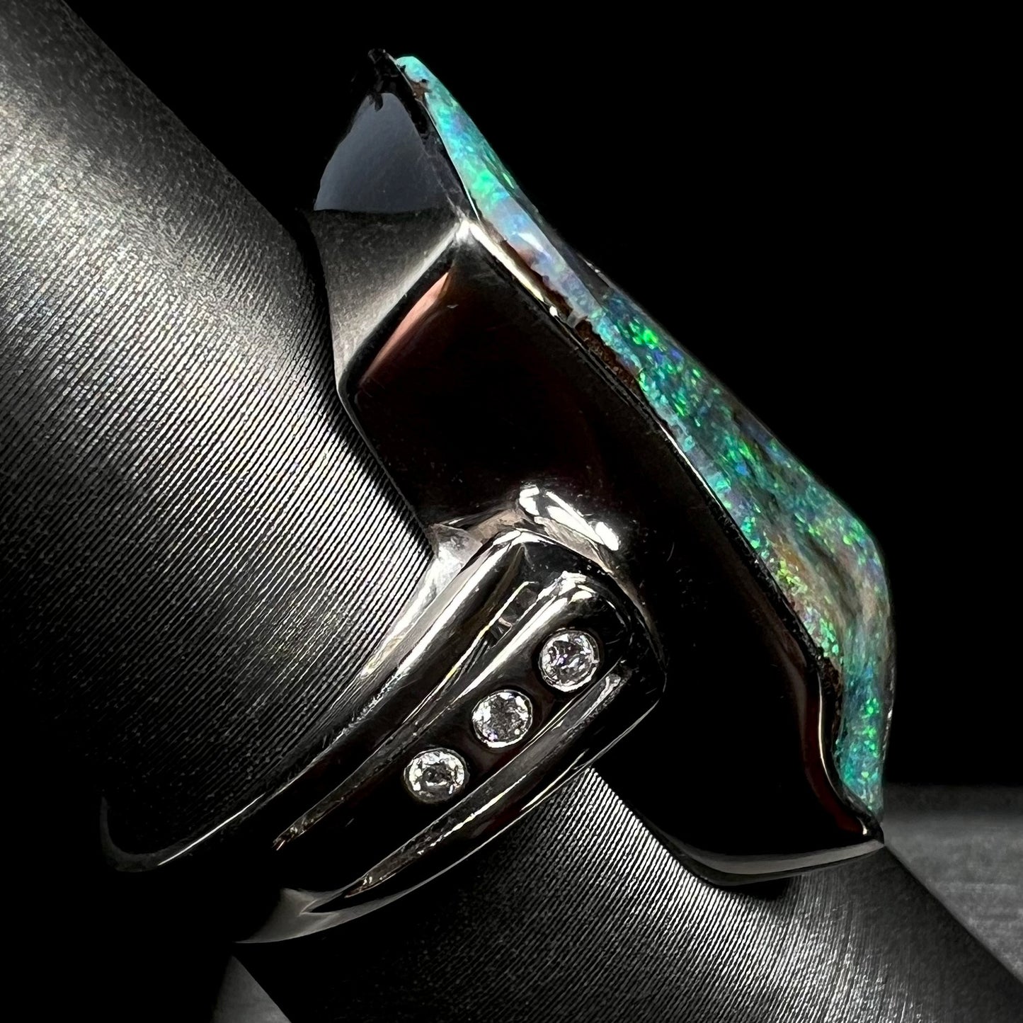 Side view of a platinum and diamond-accented boulder opal ring on a ring display.  Three diamonds are visible.