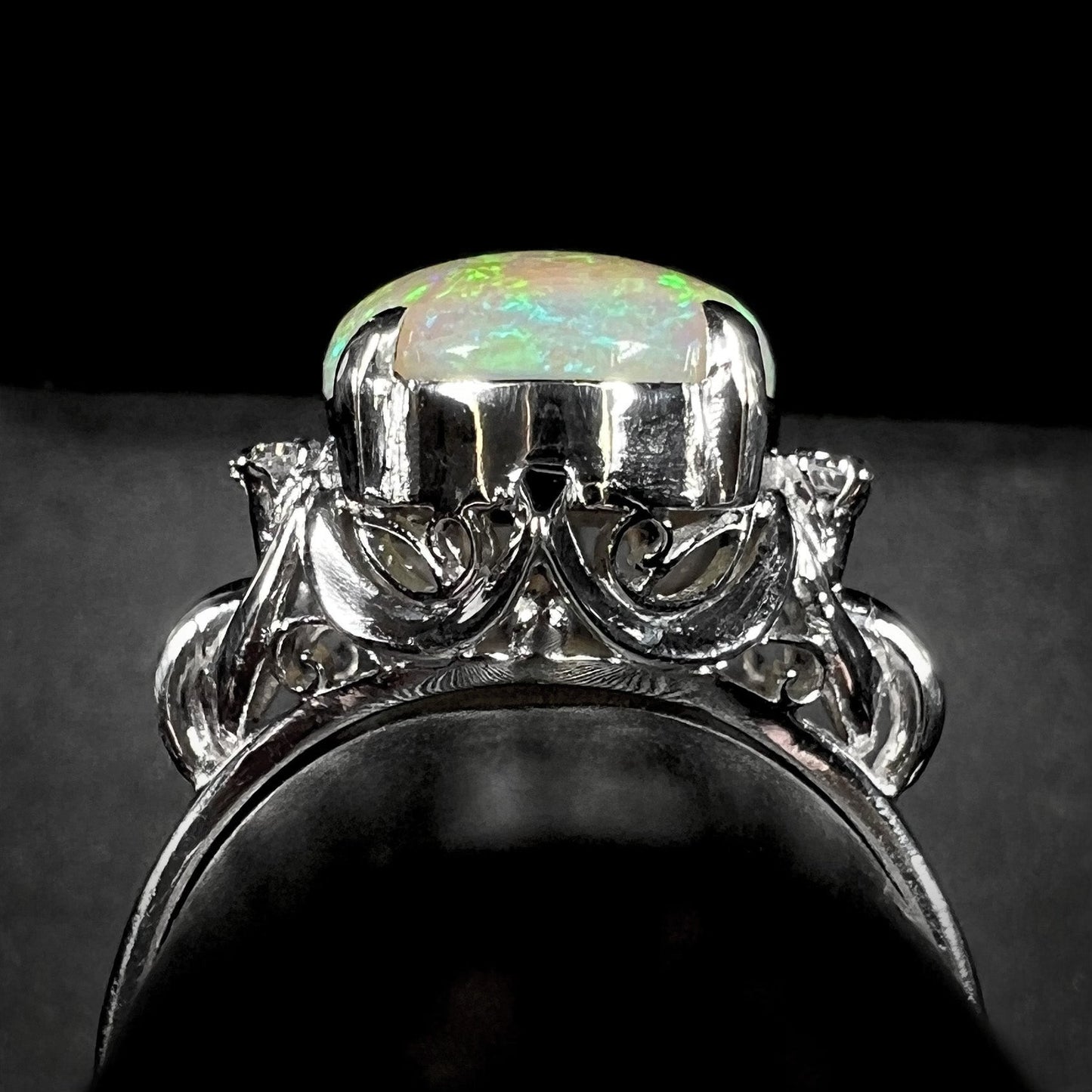An Australian crystal opal and diamond engagement ring set in a platinum filigree mounting. The opal plays green/blue colors and has a crack.