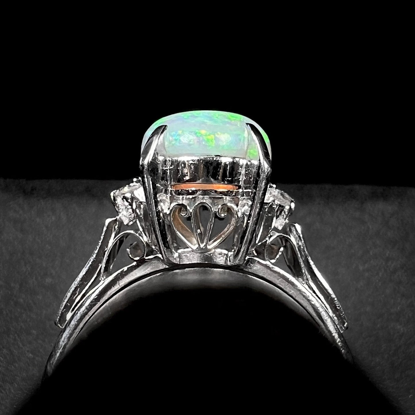 A platinum filigree opal engagement ring set with diamond accents. The opal has green-blue colors.