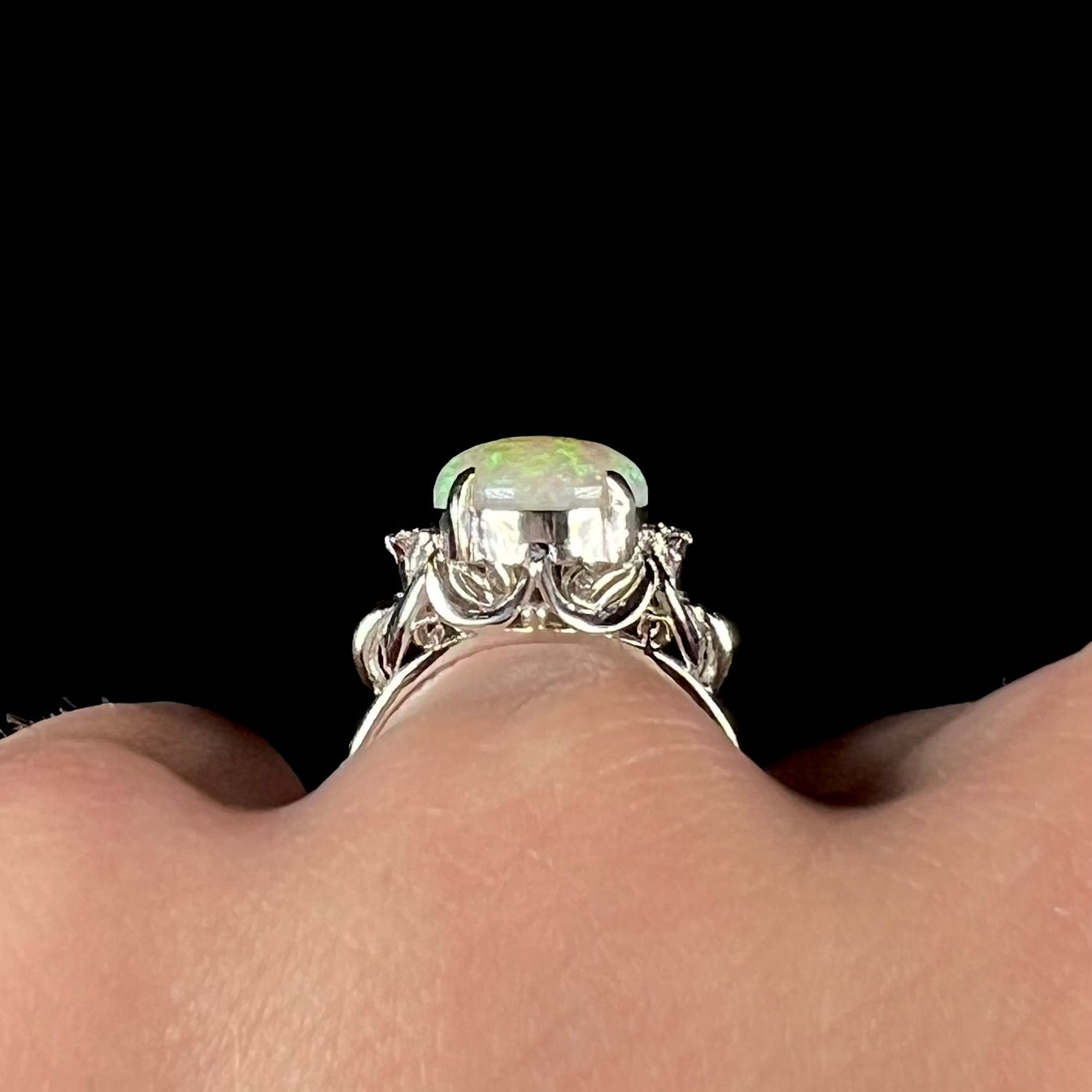 An Australian crystal opal and diamond engagement ring set in a platinum filigree mounting. The opal plays green/blue colors and has a crack.