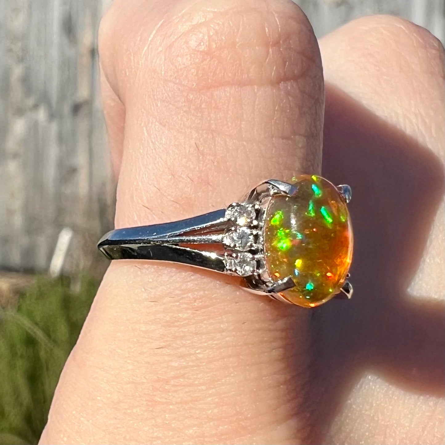 A platinum filigree and diamond-accented Mexican fire opal ring. The opal is orange with green fire.