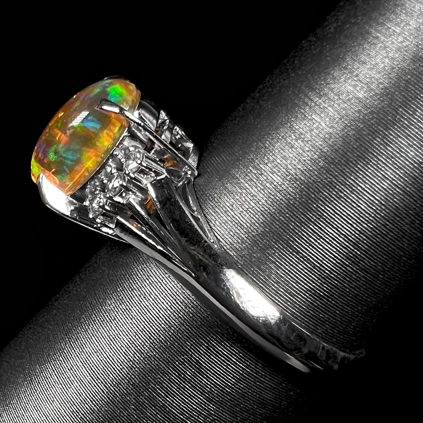 A platinum filigree and diamond-accented Mexican fire opal ring. The opal is orange with green fire.