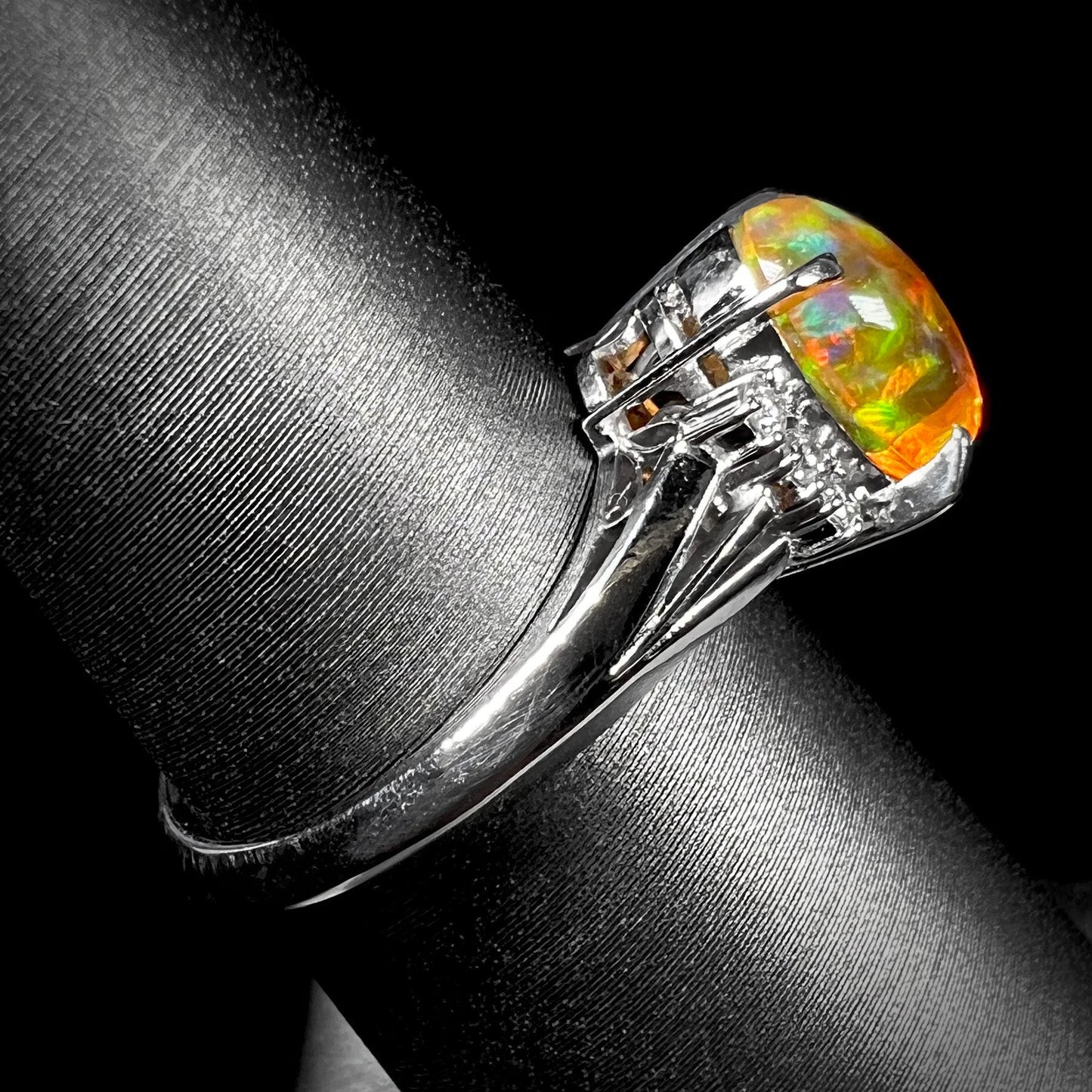 A platinum filigree and diamond-accented Mexican fire opal ring. The opal is orange with green fire.