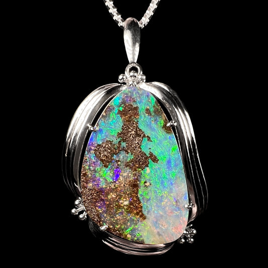 Macro view of a 14.61ct freeform boulder opal pendant in platinum with vibrant green and blue fire.