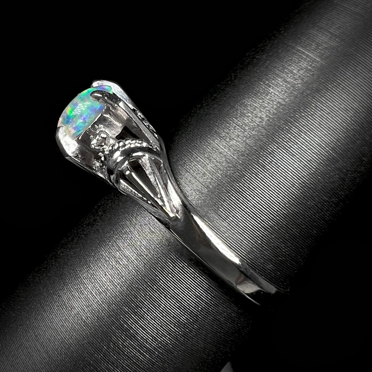The side angle of a platinum jelly opal and diamond ring. The ring has a decorative rope design.