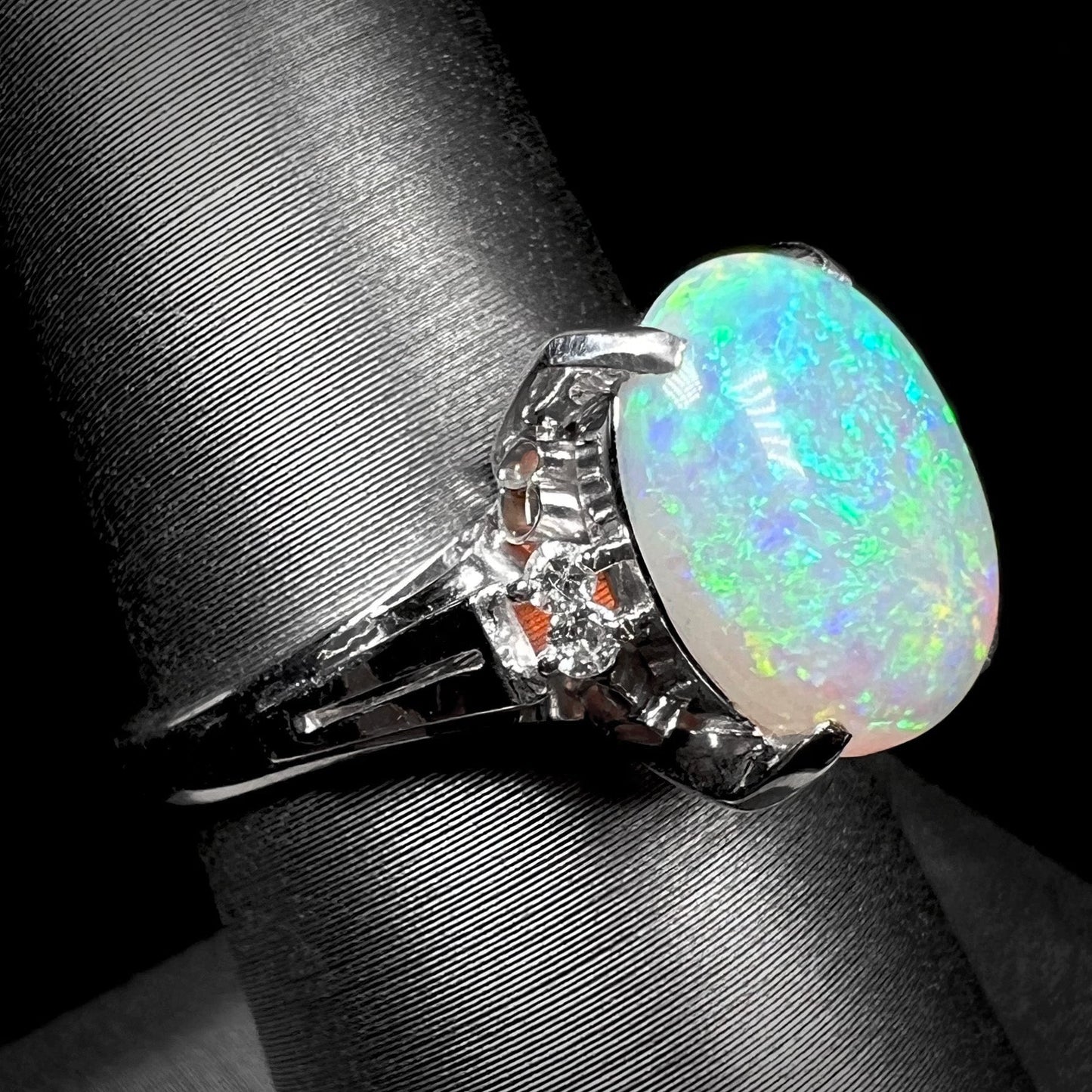 A platinum filigree opal engagement ring set with diamond accents. The opal has green-blue colors.