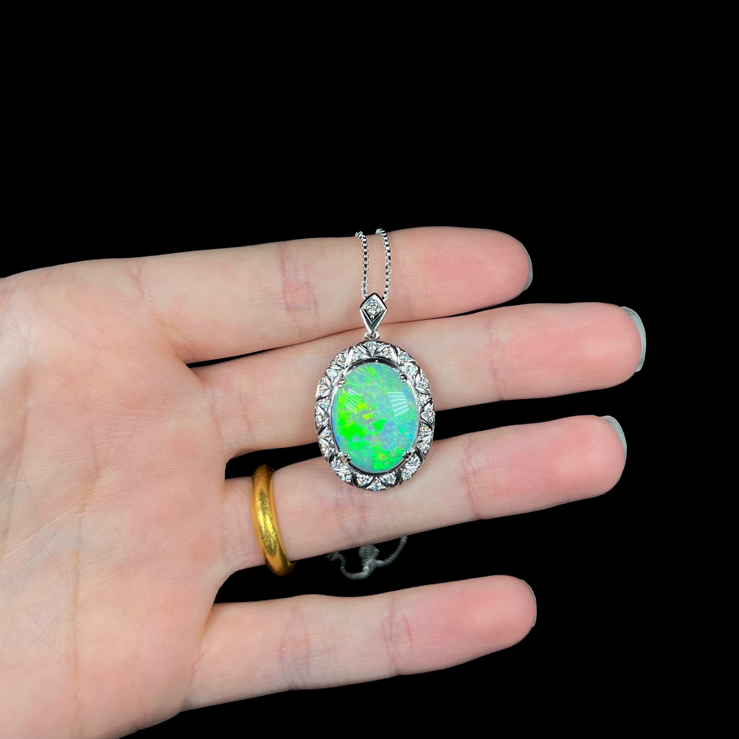 Art Deco crystal opal necklace resting on fingers with vivid green fire.