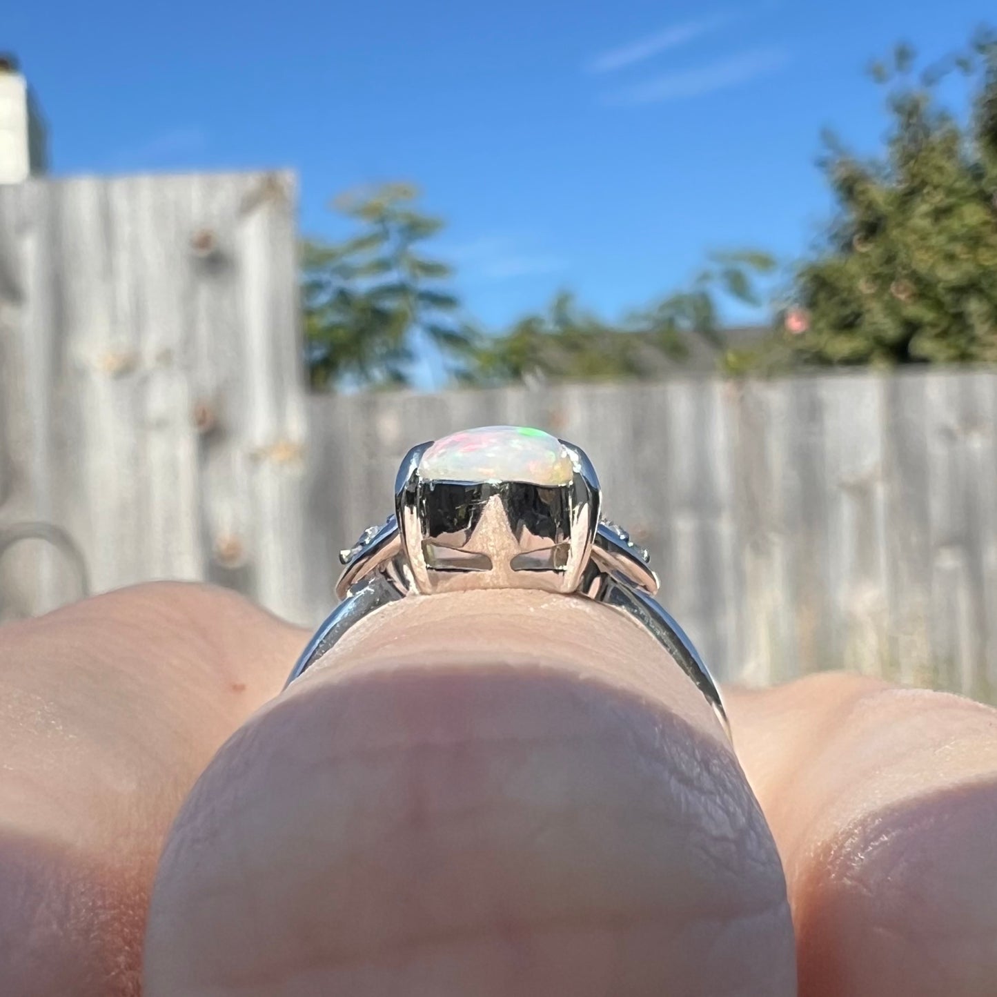 A Coober Pedy white opal platinum ring set with diamond accents. The opal plays soft pink colors.