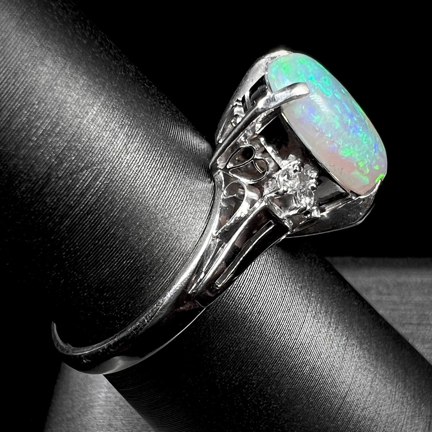 A platinum filigree opal engagement ring set with diamond accents. The opal has green-blue colors.