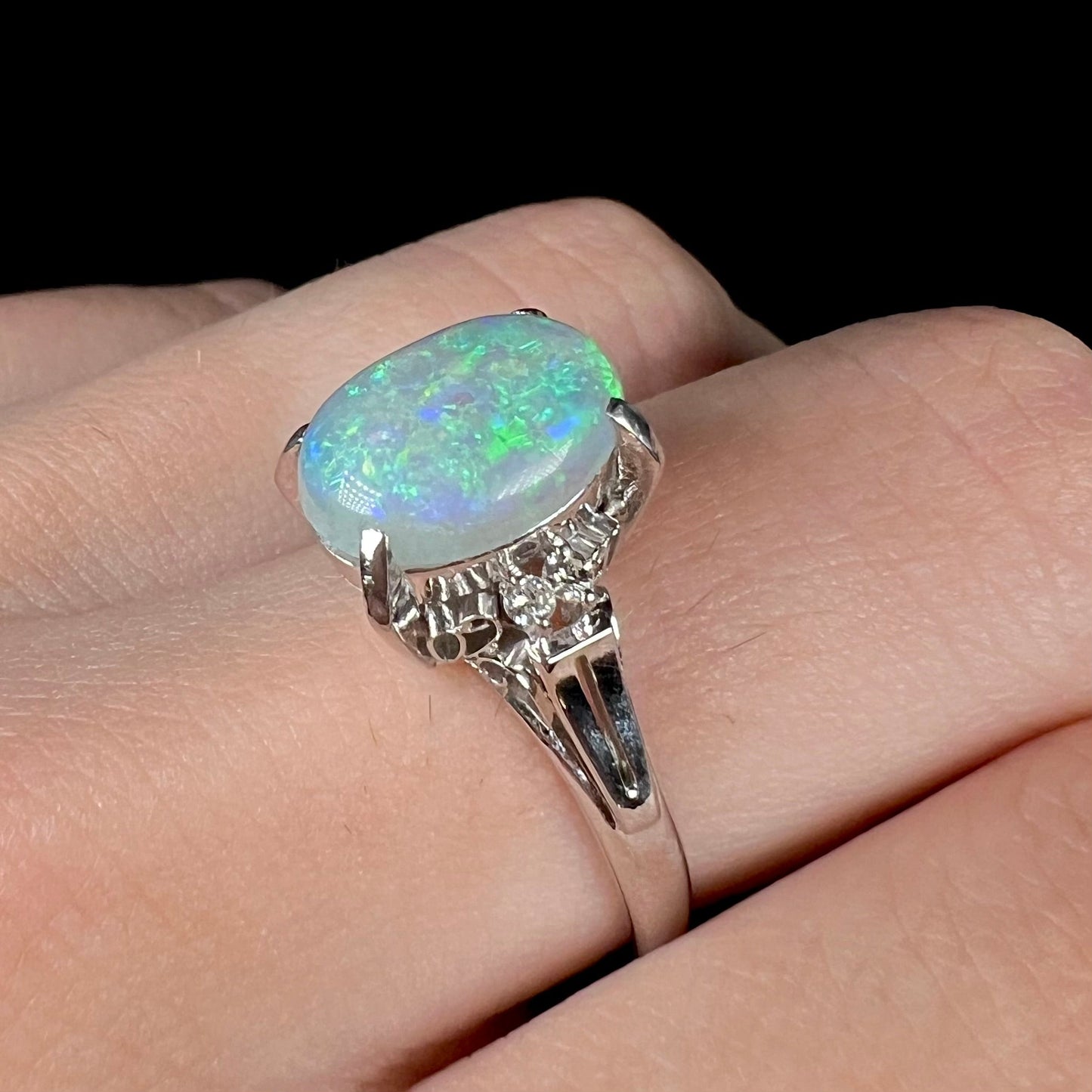 A platinum filigree opal engagement ring set with diamond accents. The opal has green-blue colors.