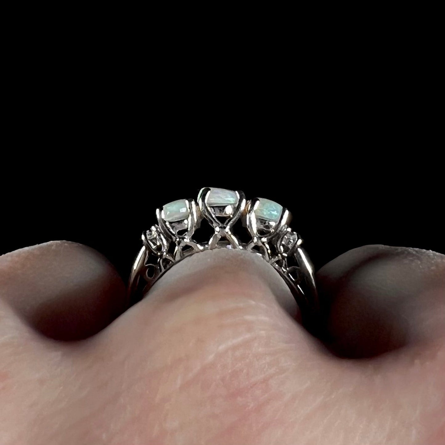 A ladies' white gold ring prong-set with three natural white opals and diamond accents. The opals play a green color.