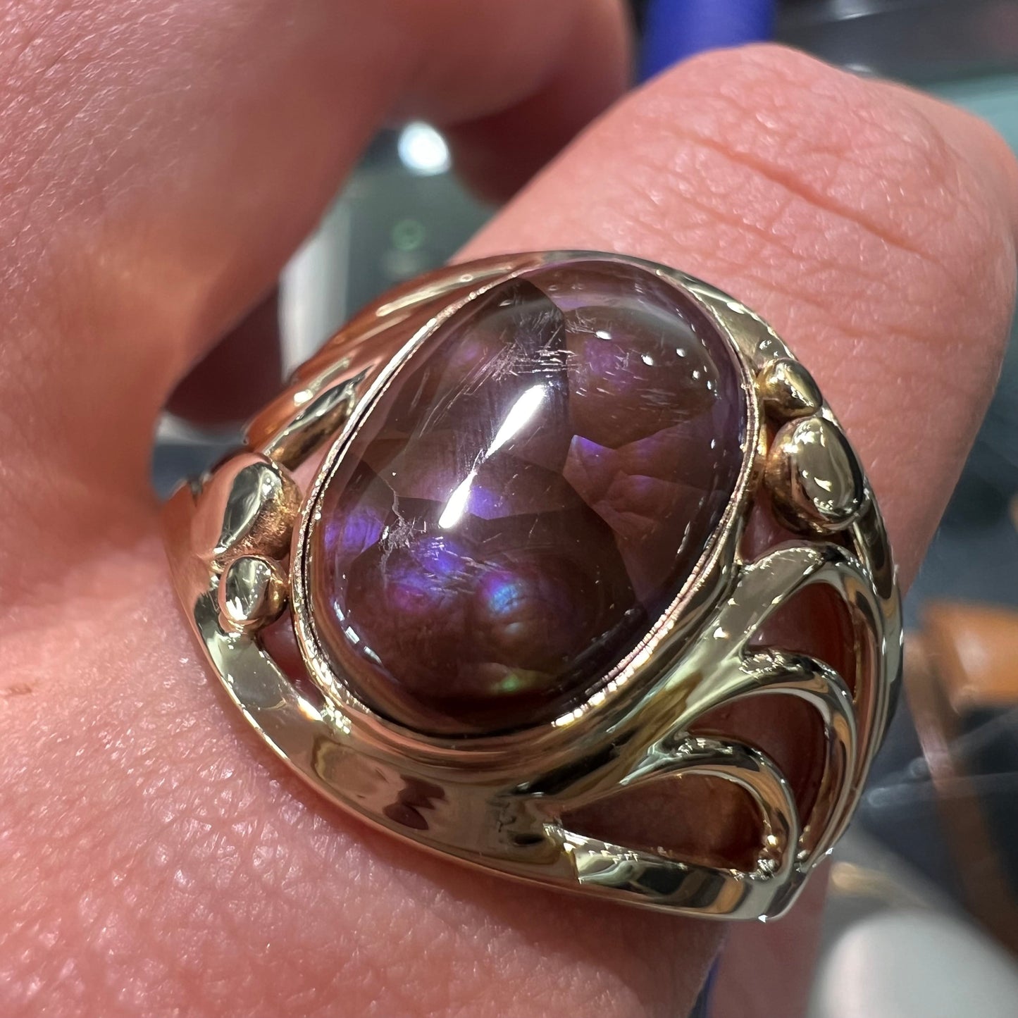 An oval cabochon cut fire agate with purple and blue colors set in a yellow gold men's ring.