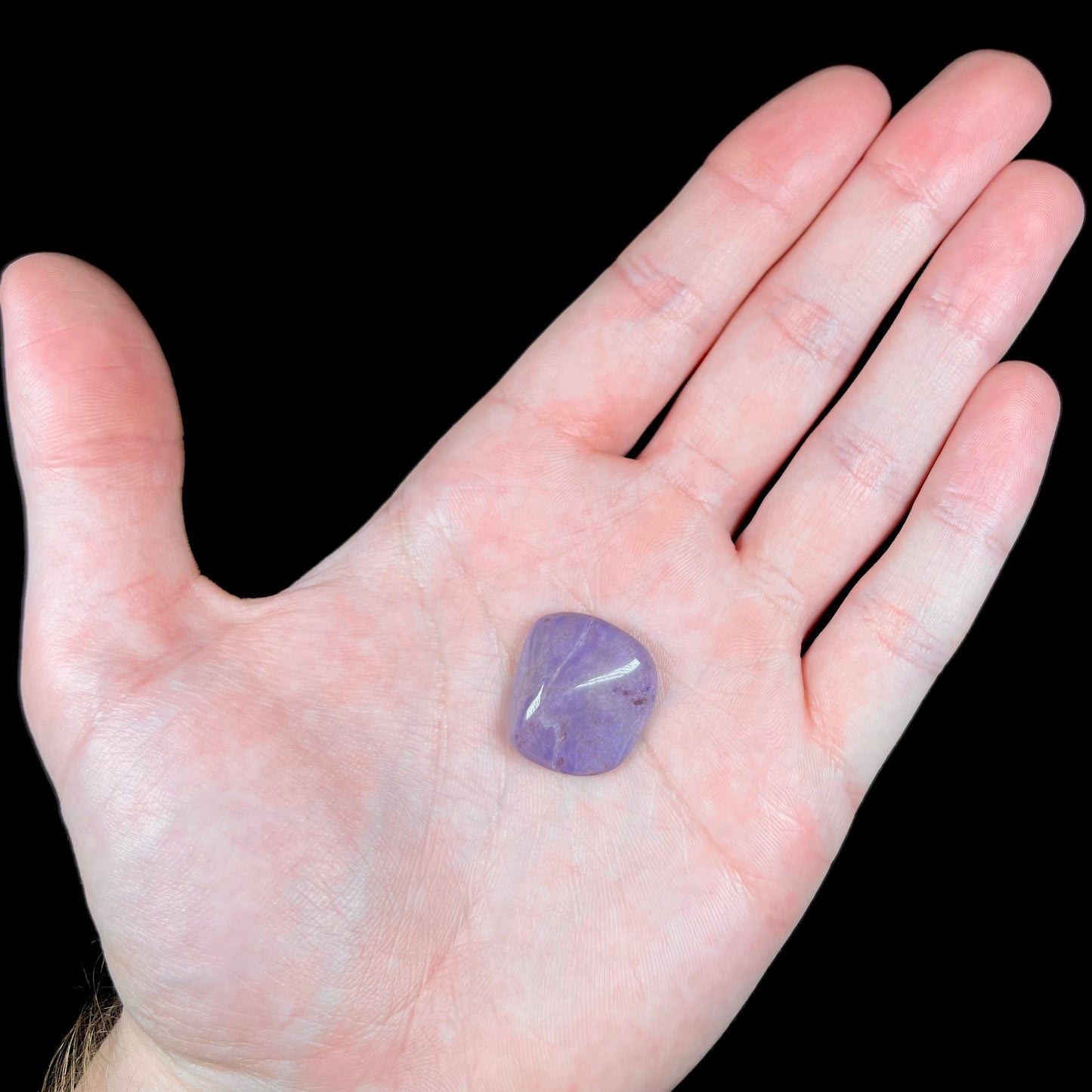 A tumbled turkiyenite jade stone from Bursa, Turkey. The rock is purple with red speckles.