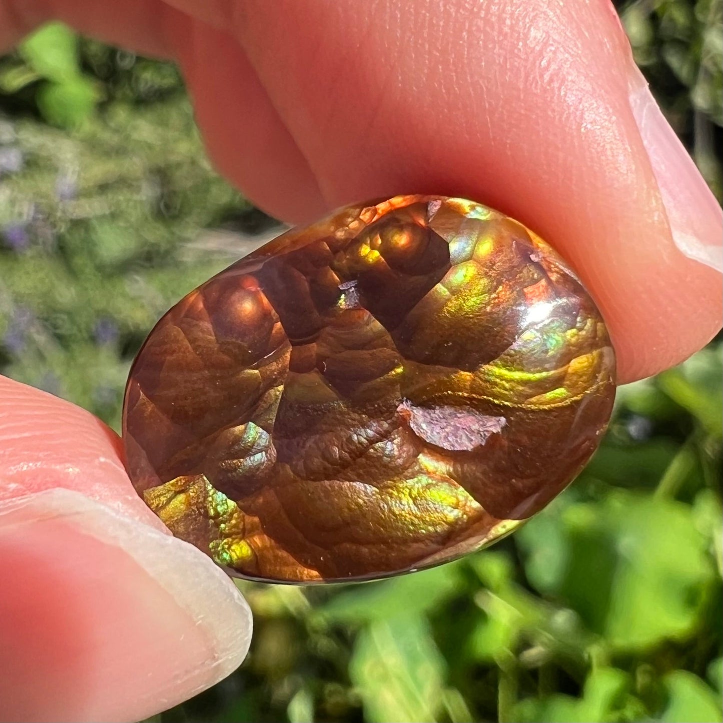 An oval cabochon cut Mexican fire agate stone. The stone's predominant colors are green, yellow, orange, and blue.