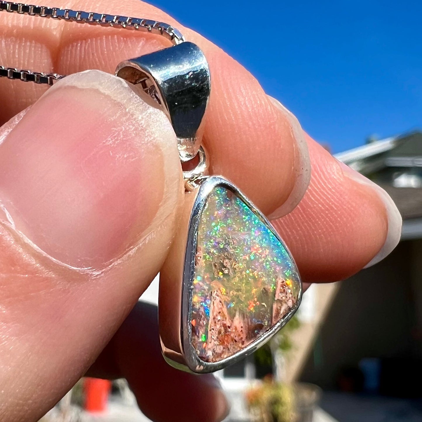 A sterling silver boulder opal necklace on a box chain. The opal twinkles bright red, green, and blue colors.