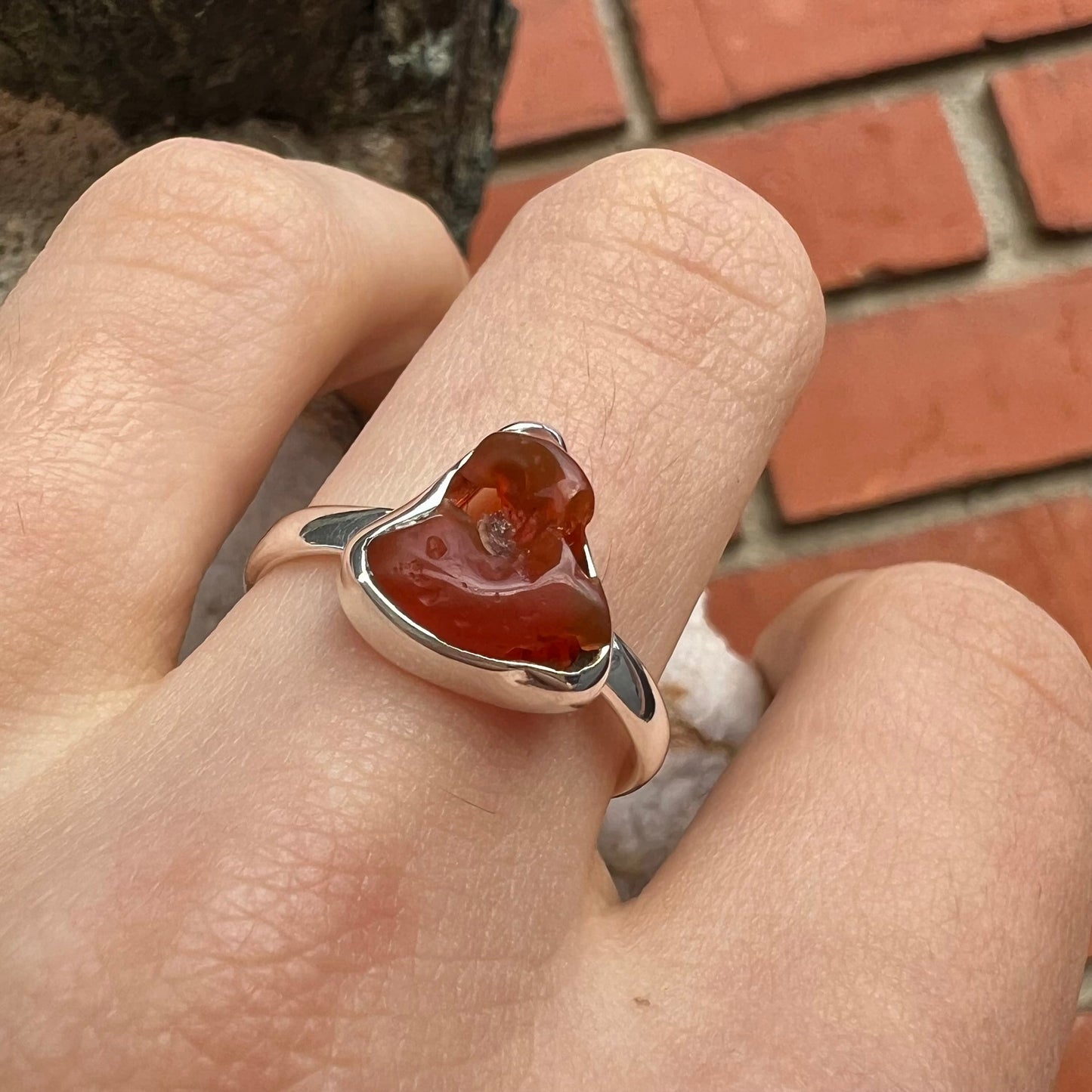 A polished fire opal crystal bezel set into a sterling silver ring. The opal is an orange color.