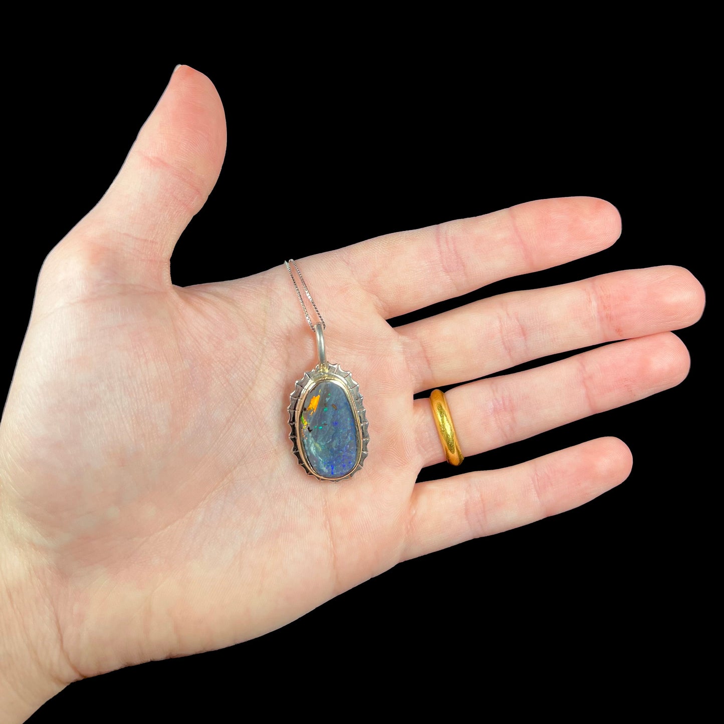 A Southwest style two-tone sterling silver pendant set with a black boulder opal with a yellow gold bezel.