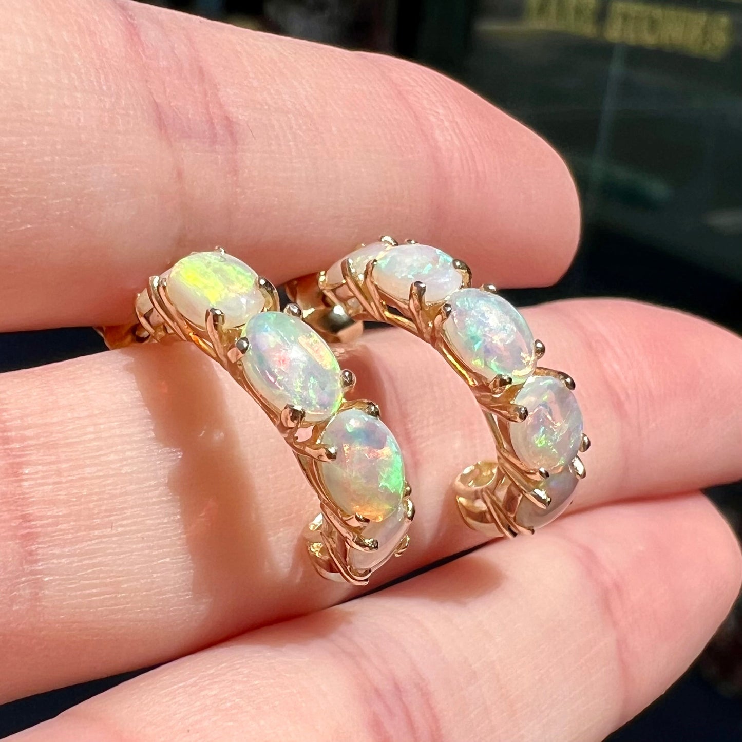 A pair of yellow gold opal hoop earrings. Each earring is set with six natural oval cut opals.