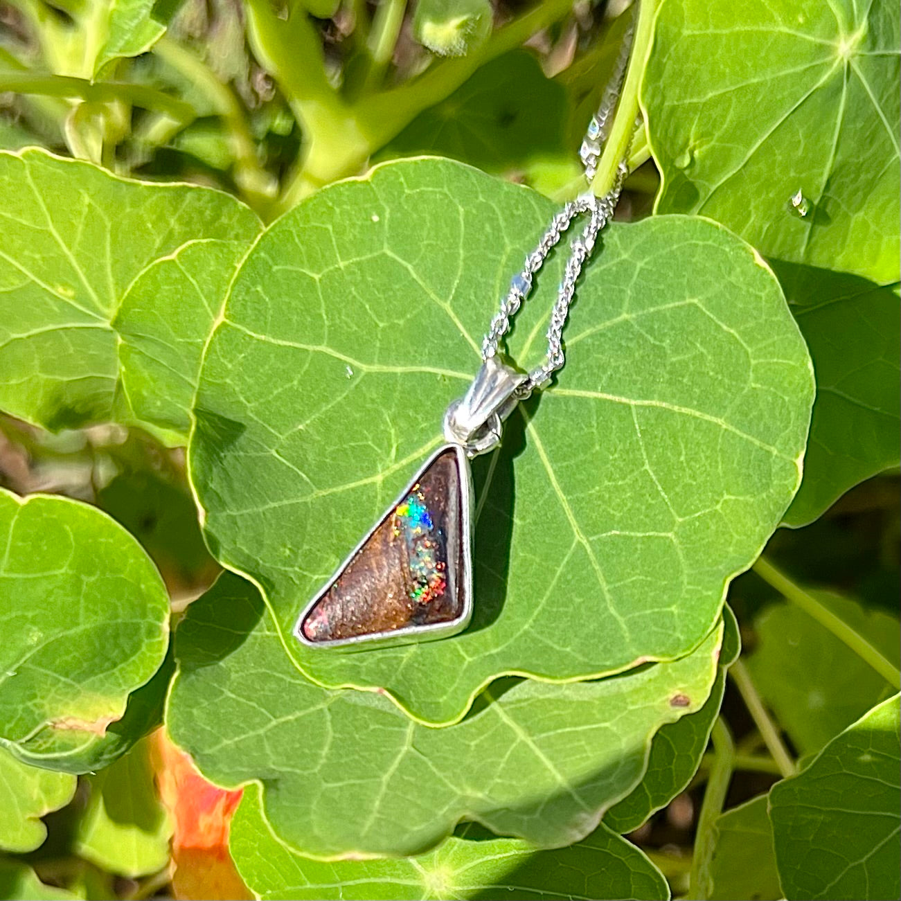 A sterling silver necklace bezel set with a triangle shaped boulder opal.  The opal has red and blue flashes.