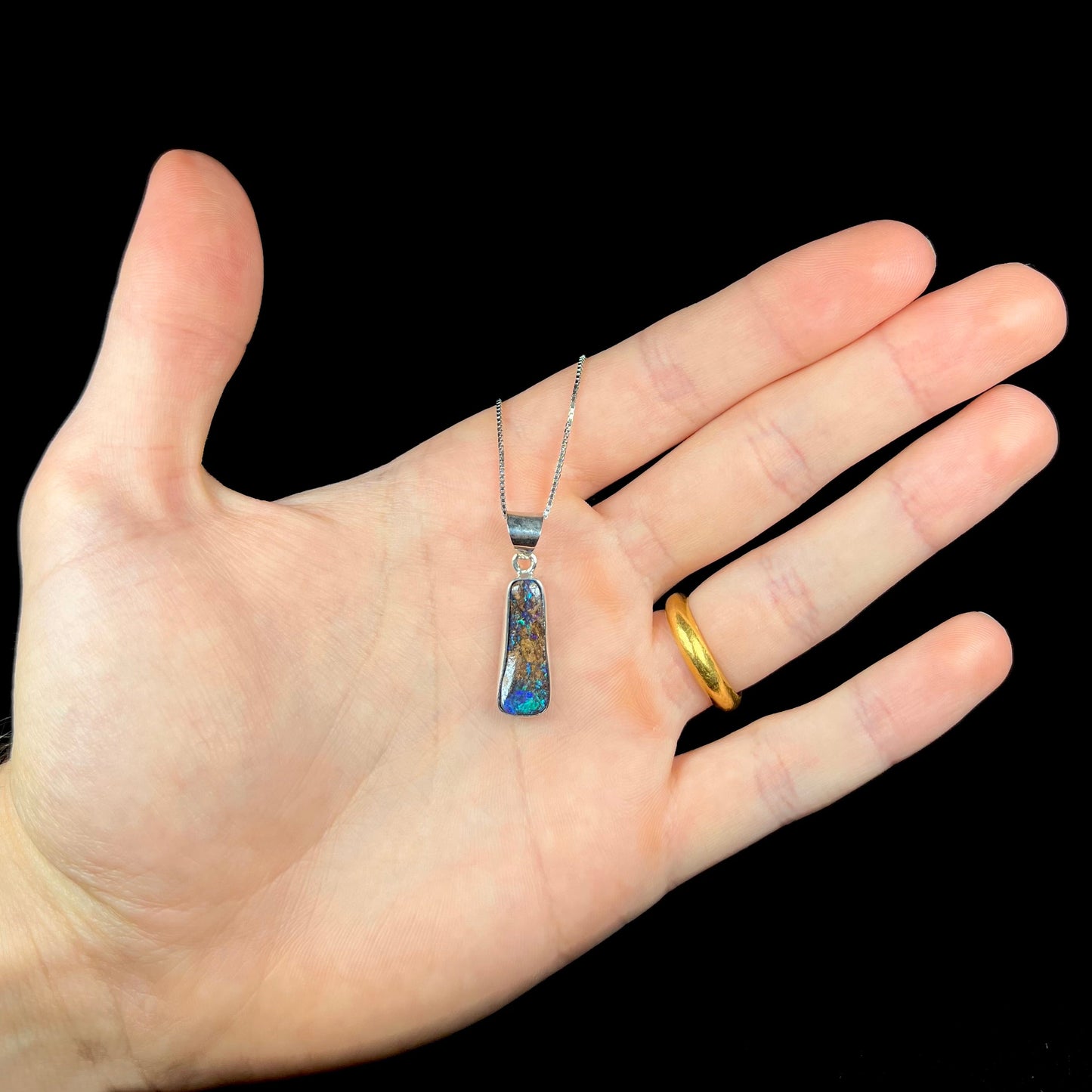 A sterling silver necklace bezel set with a natural Australian boulder opal stone. The stone shines colors of blue, green, and purple.