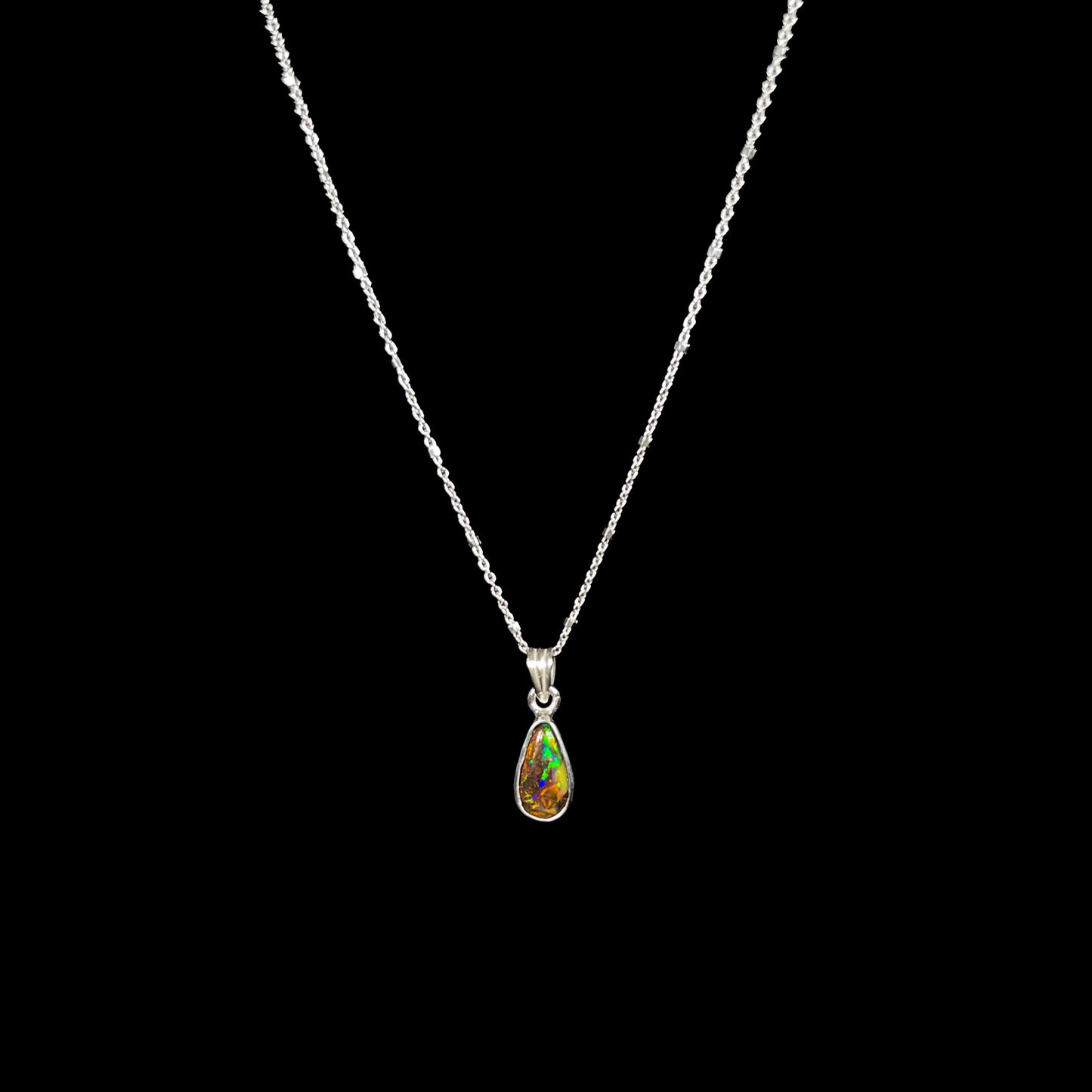 A natural, pear shaped Australian boulder opal with blue, purple, and green colors bezel set into a sterling silver necklace.