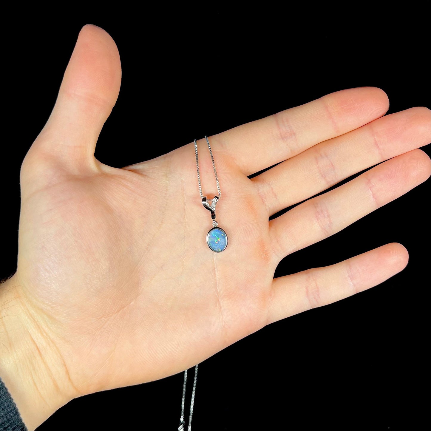 A sterling silver necklace set with a natural black opal doublet and white zircon accent stones.